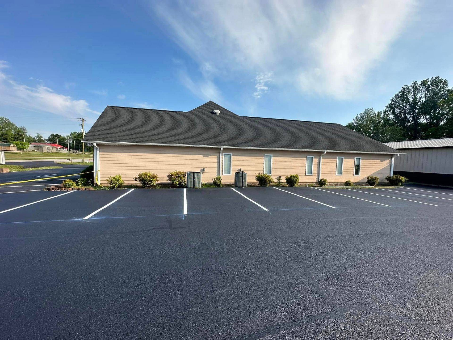Building with asphalt parking lot under a blue sky; shrubs and parking space lines visible.