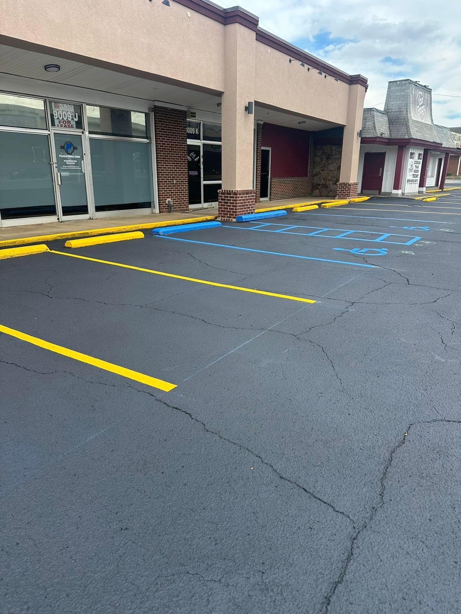 Asphalt parking lot with yellow and blue painted lines in front of a retail building.
