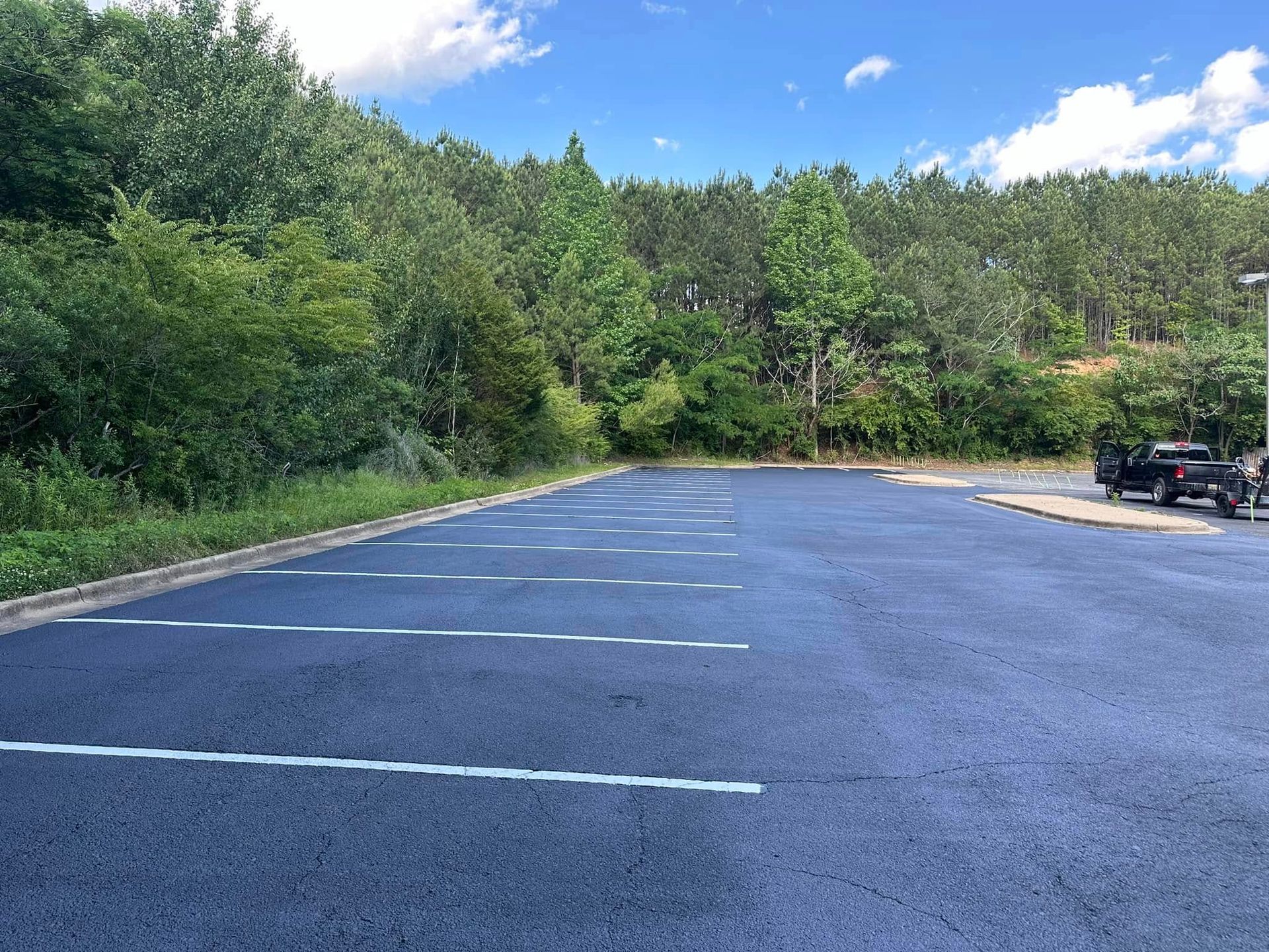 Empty asphalt parking lot with white lines, surrounded by trees and a blue sky.