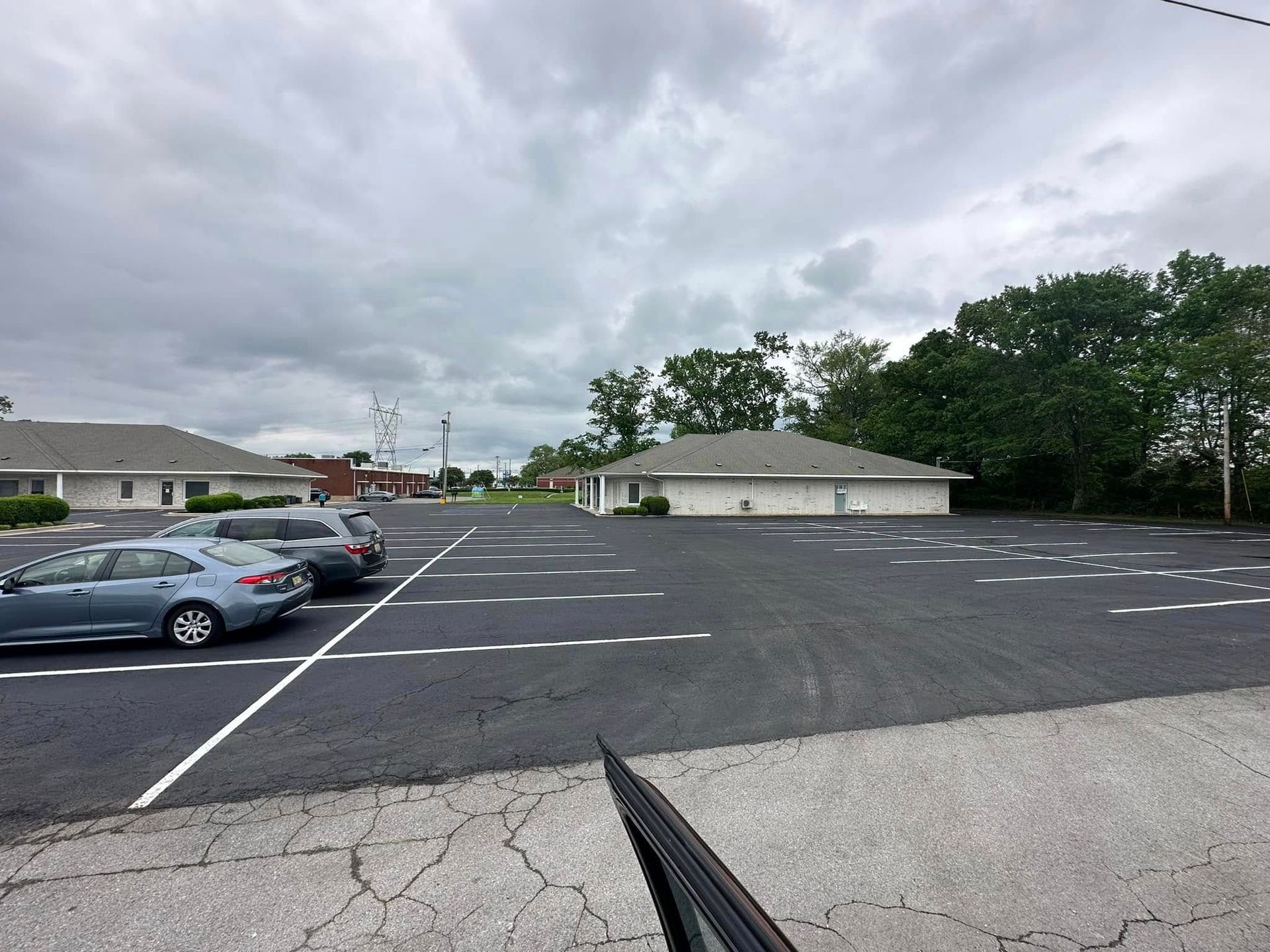 A parking lot with several parked cars in front of low-rise buildings on a cloudy day.