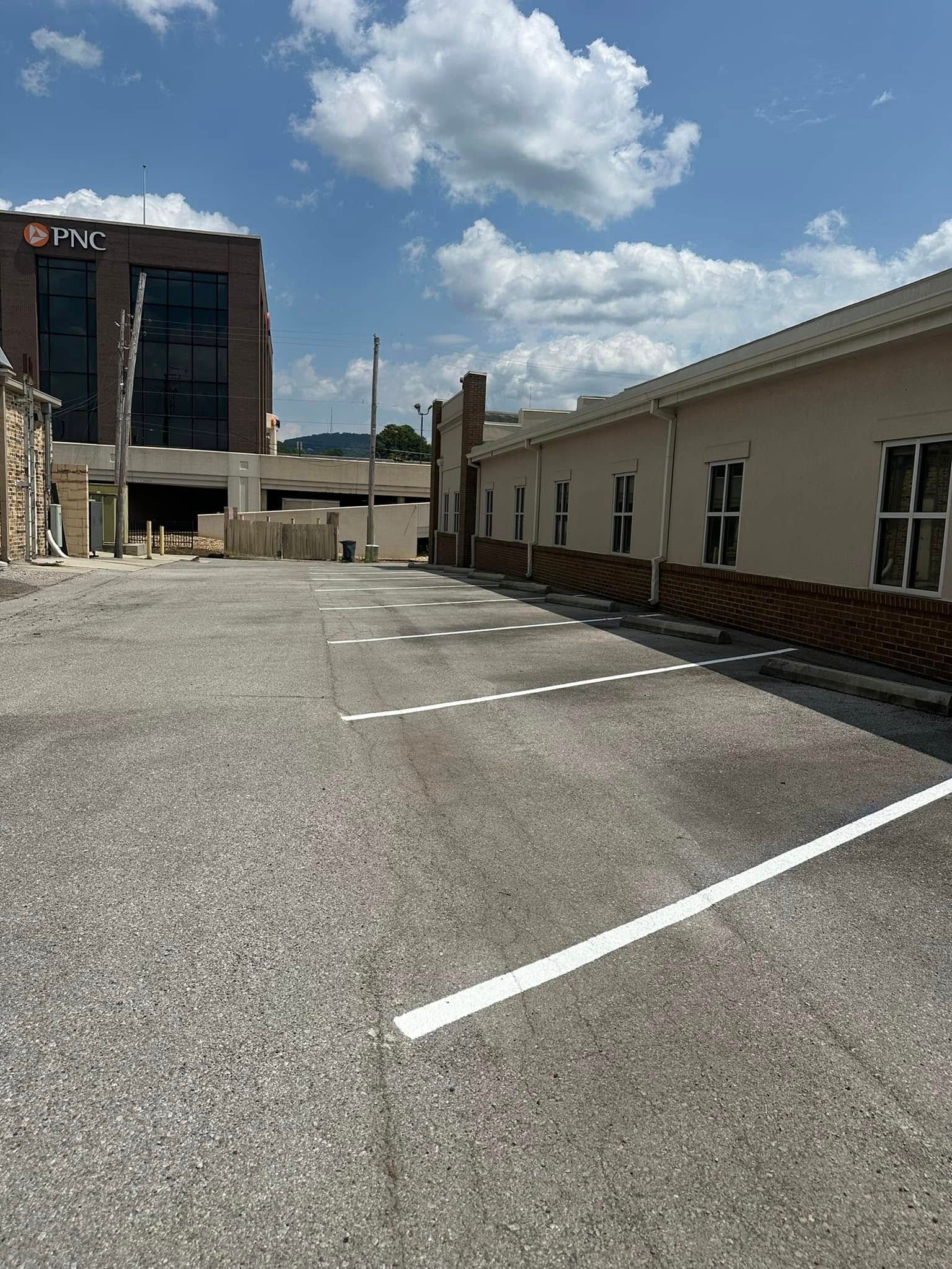 Gravel parking lot with white lines, beige building with windows on right, modern brick building on left, blue sky.