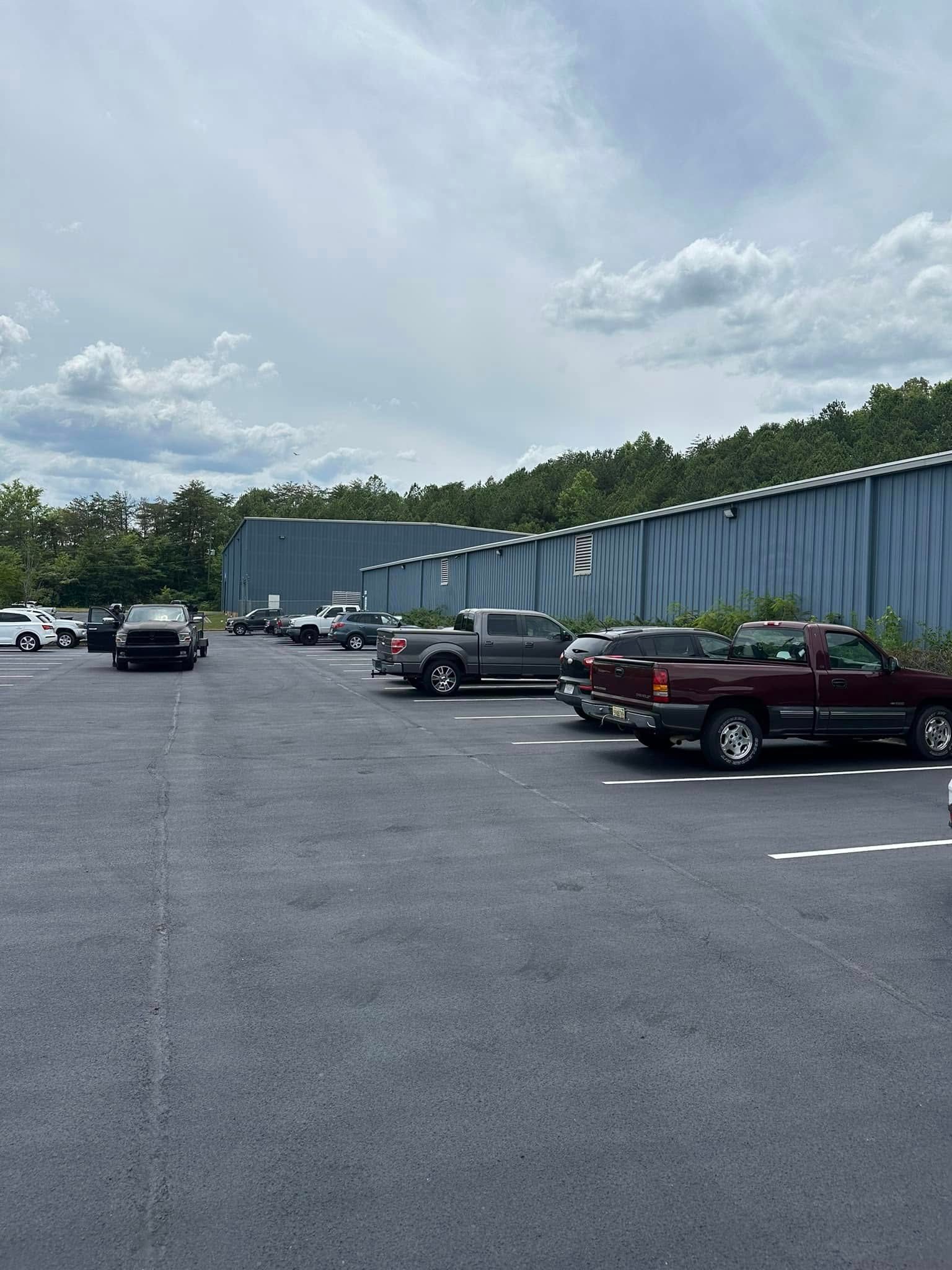 Parking lot with several pickup trucks and other vehicles, in front of a blue building under a cloudy sky.