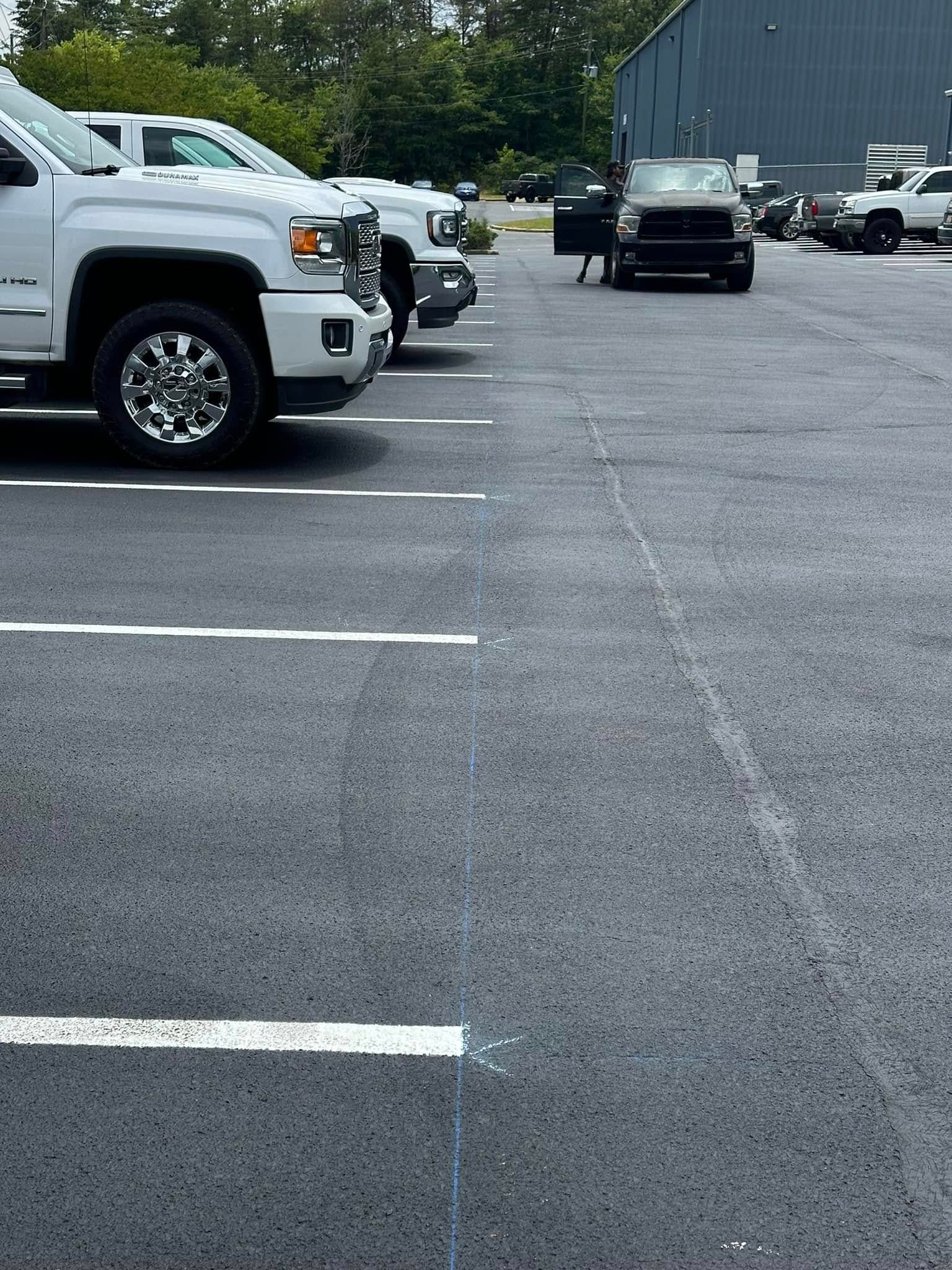 White pickup trucks parked in an asphalt parking lot. A person stands near a black truck.
