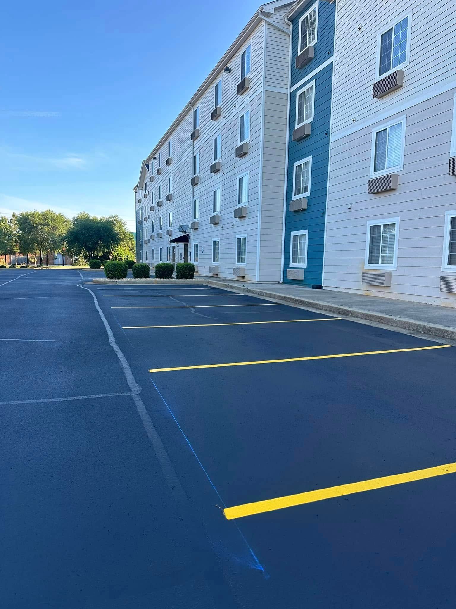 Hotel with blue and gray facade, a large asphalt parking lot, and a bright blue sky.