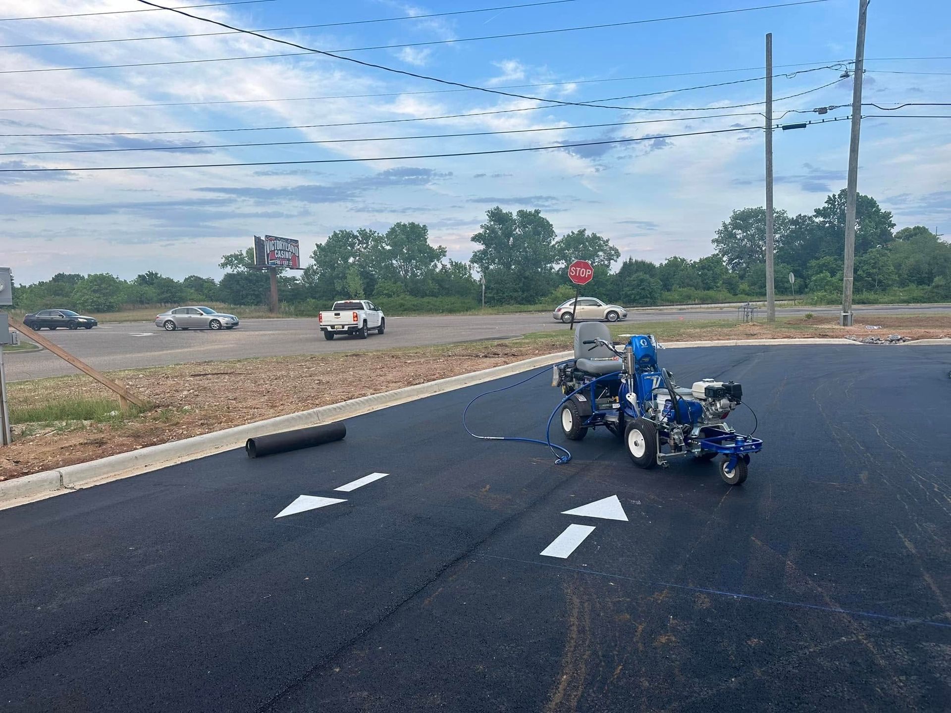 Road marking machine painting white arrows on black asphalt, roadside with traffic.
