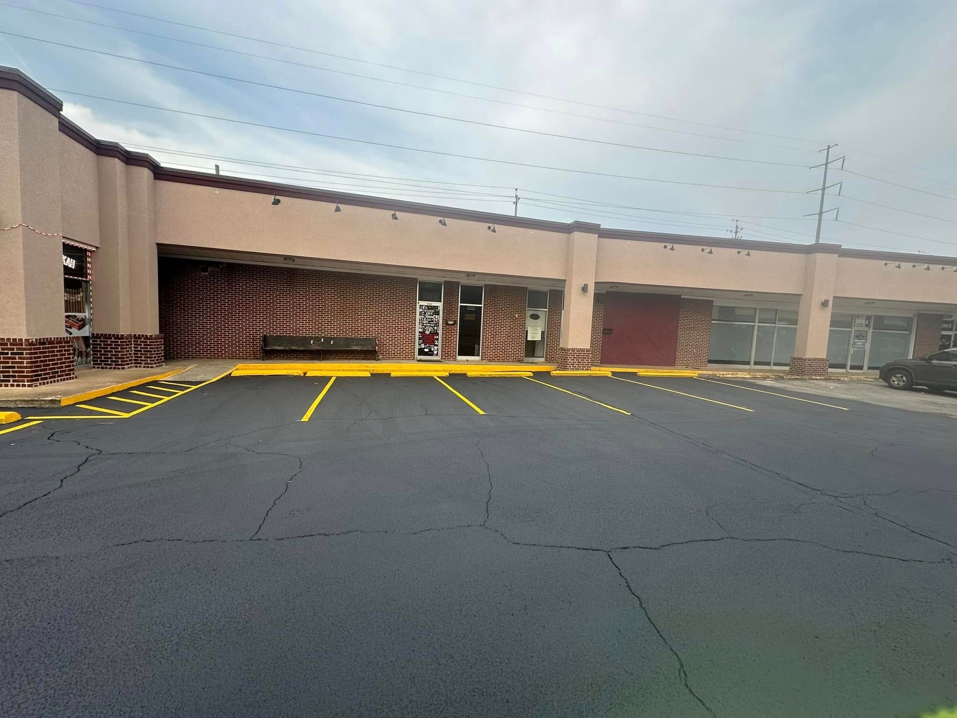 Exterior of a strip mall with a freshly paved asphalt parking lot. Building is beige with a decorative front.