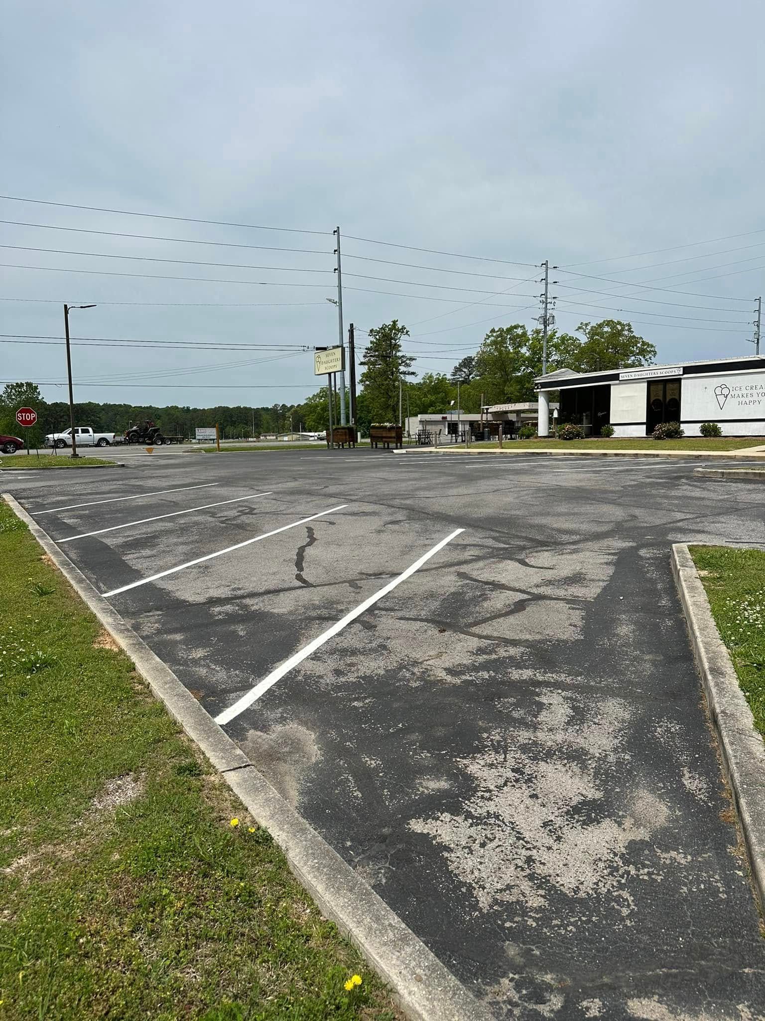 Cracked asphalt parking lot; white parking lines, building, trees, and power lines in view. Overcast sky.