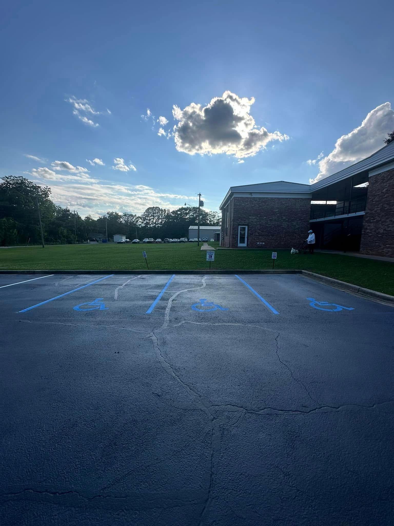 Empty parking spaces in front of a brick building and a green lawn under a partly cloudy sky.
