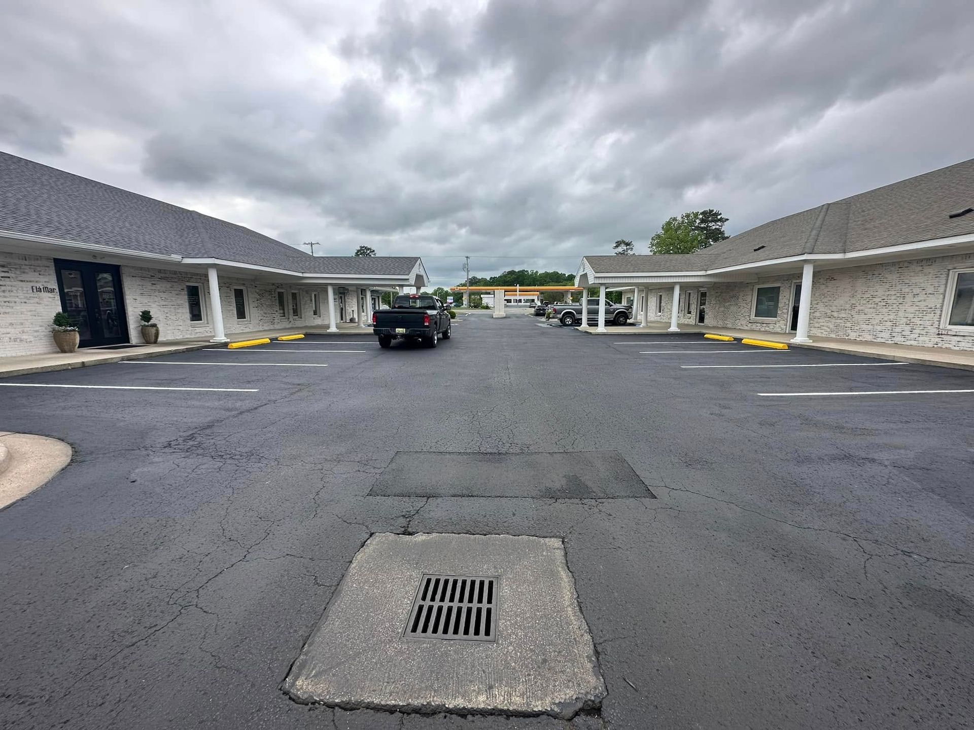 Exterior view of a motel with parked cars on a cloudy day. Asphalt parking lot with building units.