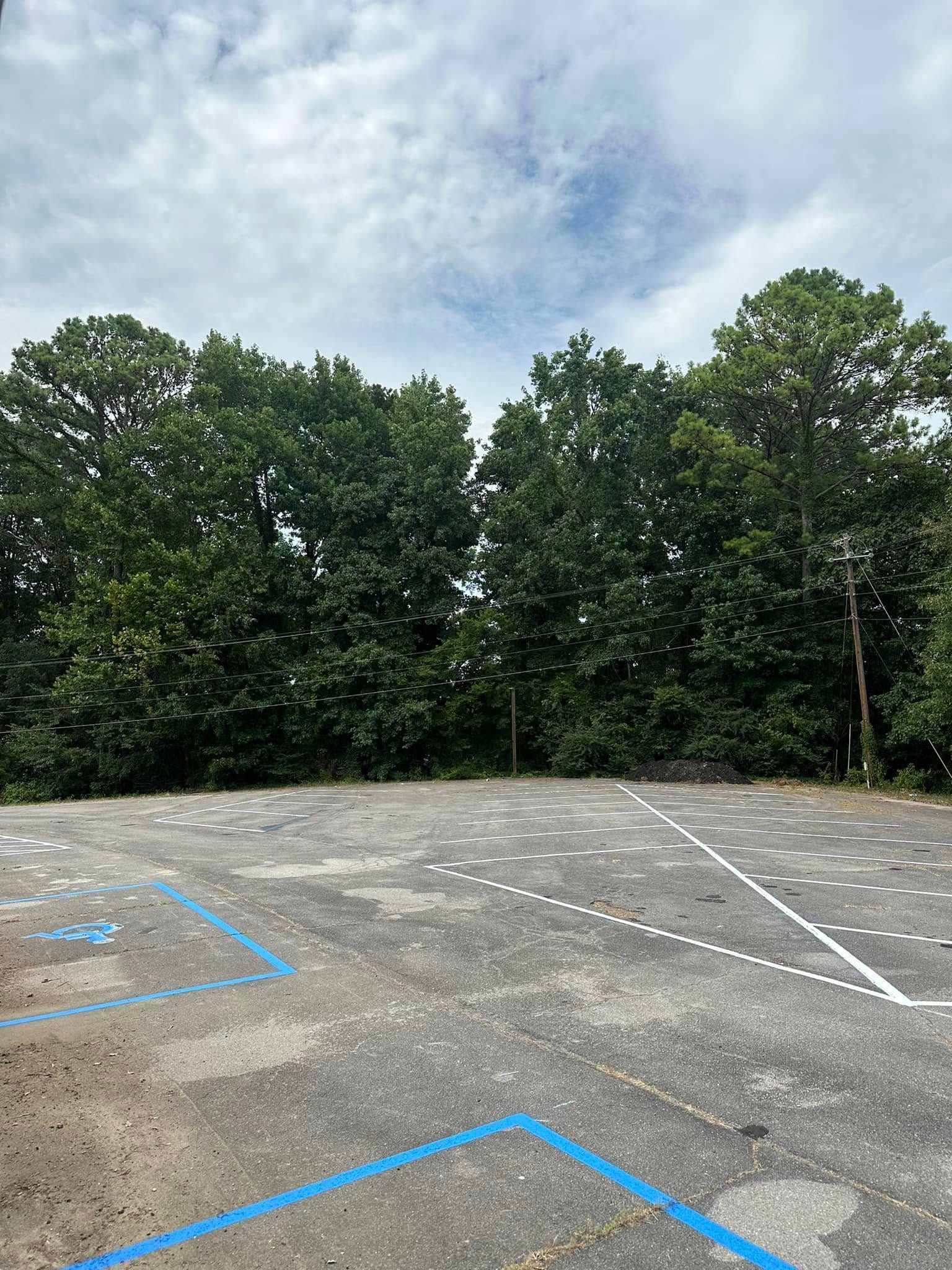 Asphalt parking lot with blue handicap markings. Trees in background, cloudy sky overhead.