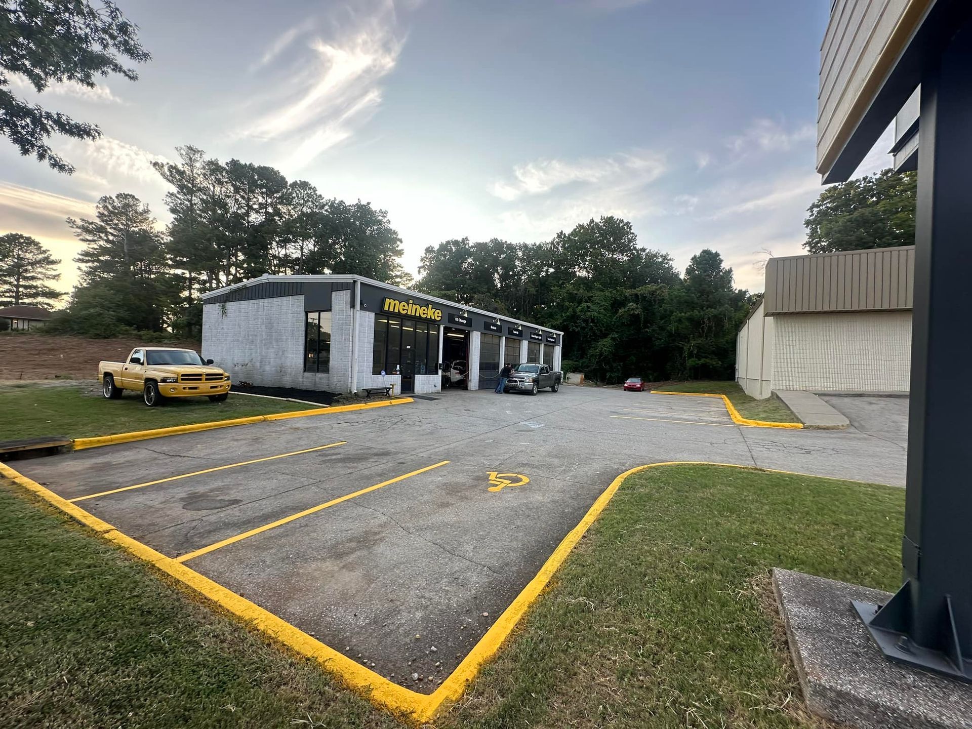 A gray and white auto repair shop with parked cars outside on a gravel lot.