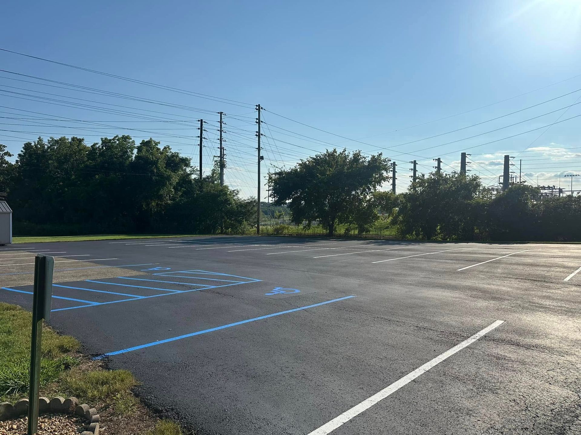 Empty asphalt parking lot with blue directional arrows, trees, and power lines against a clear blue sky.