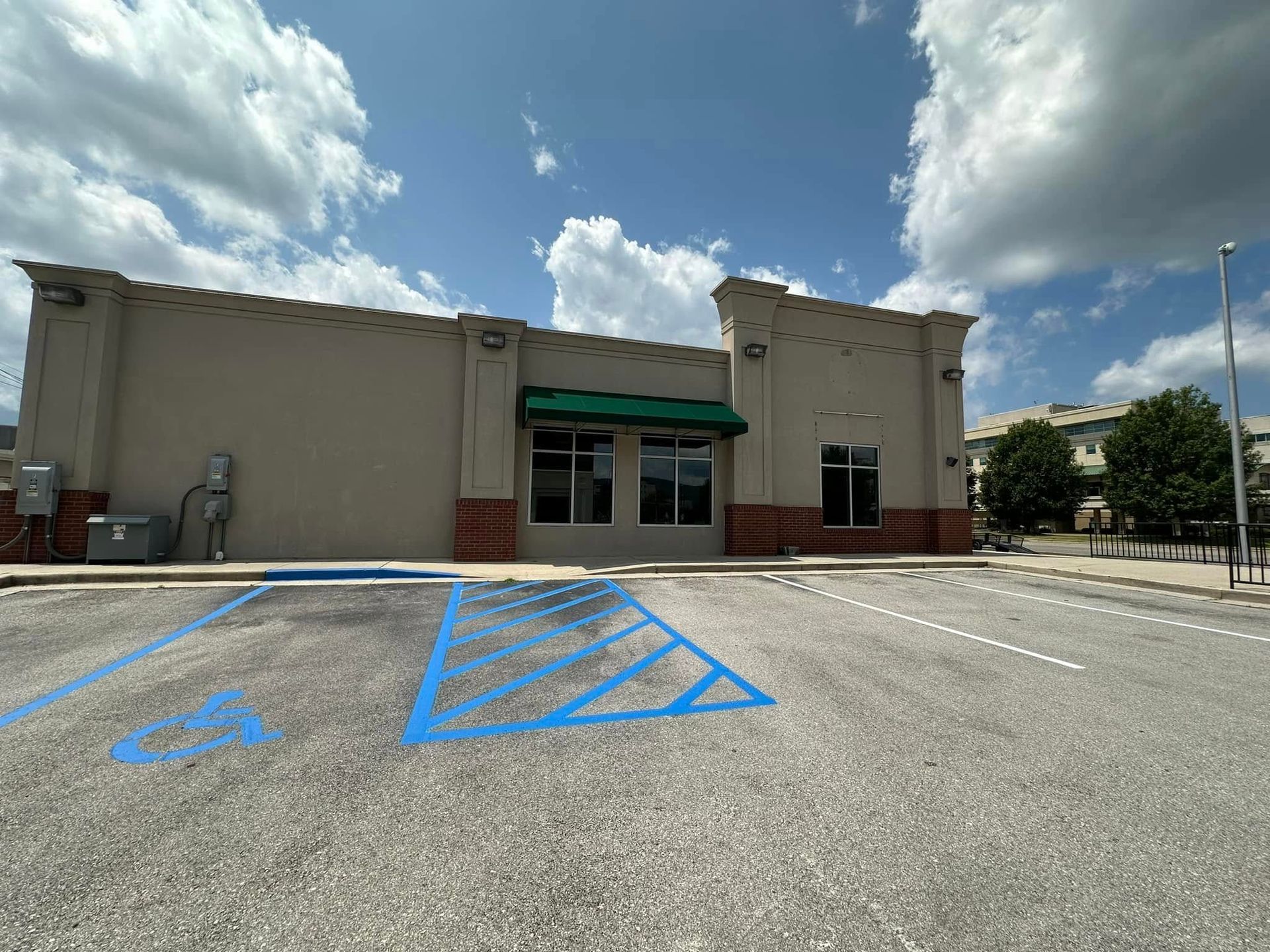 Exterior of a beige commercial building with a green awning, empty parking lot, and blue sky.