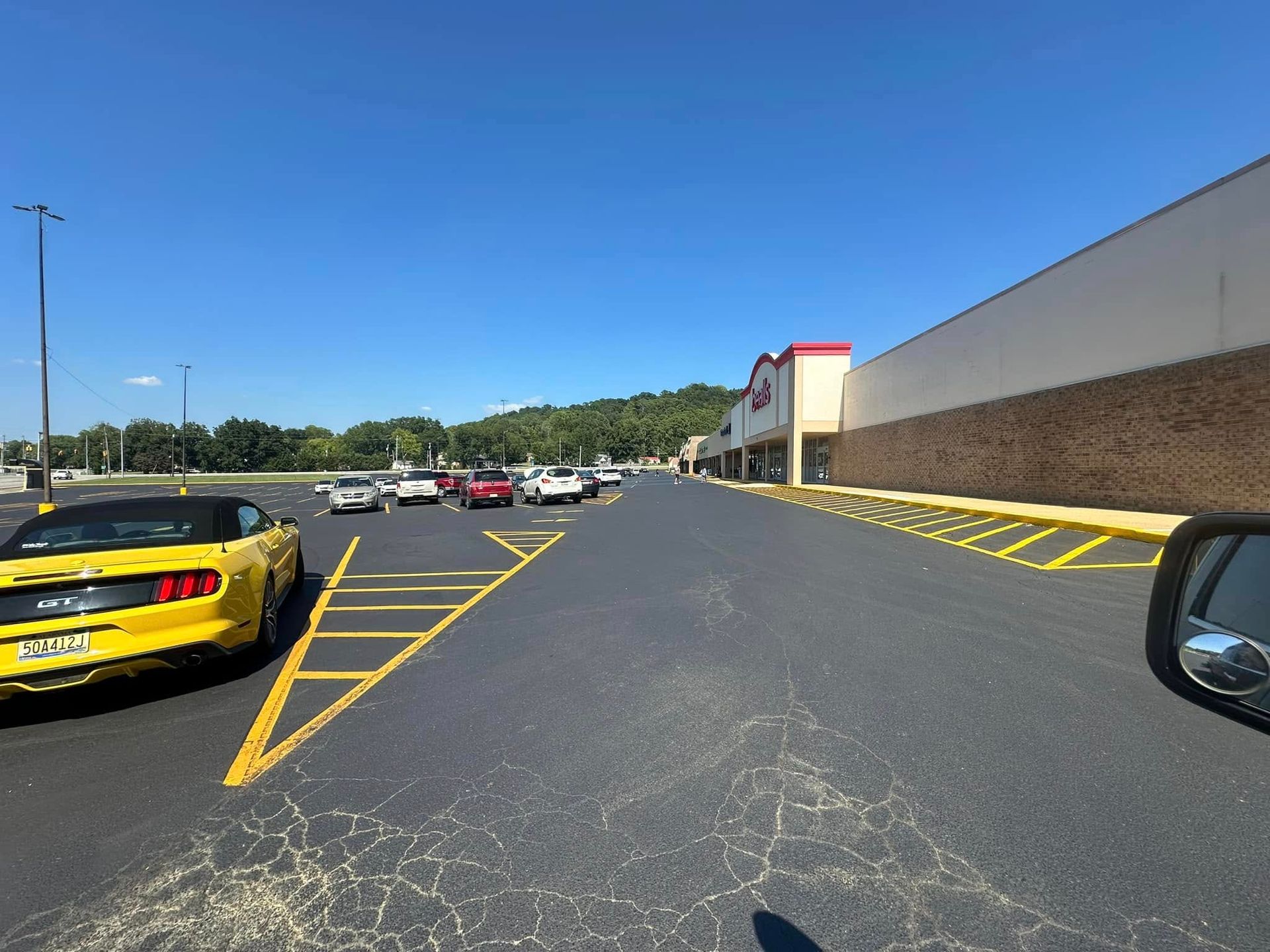 Yellow car in parking lot with other cars near a store on a sunny day.