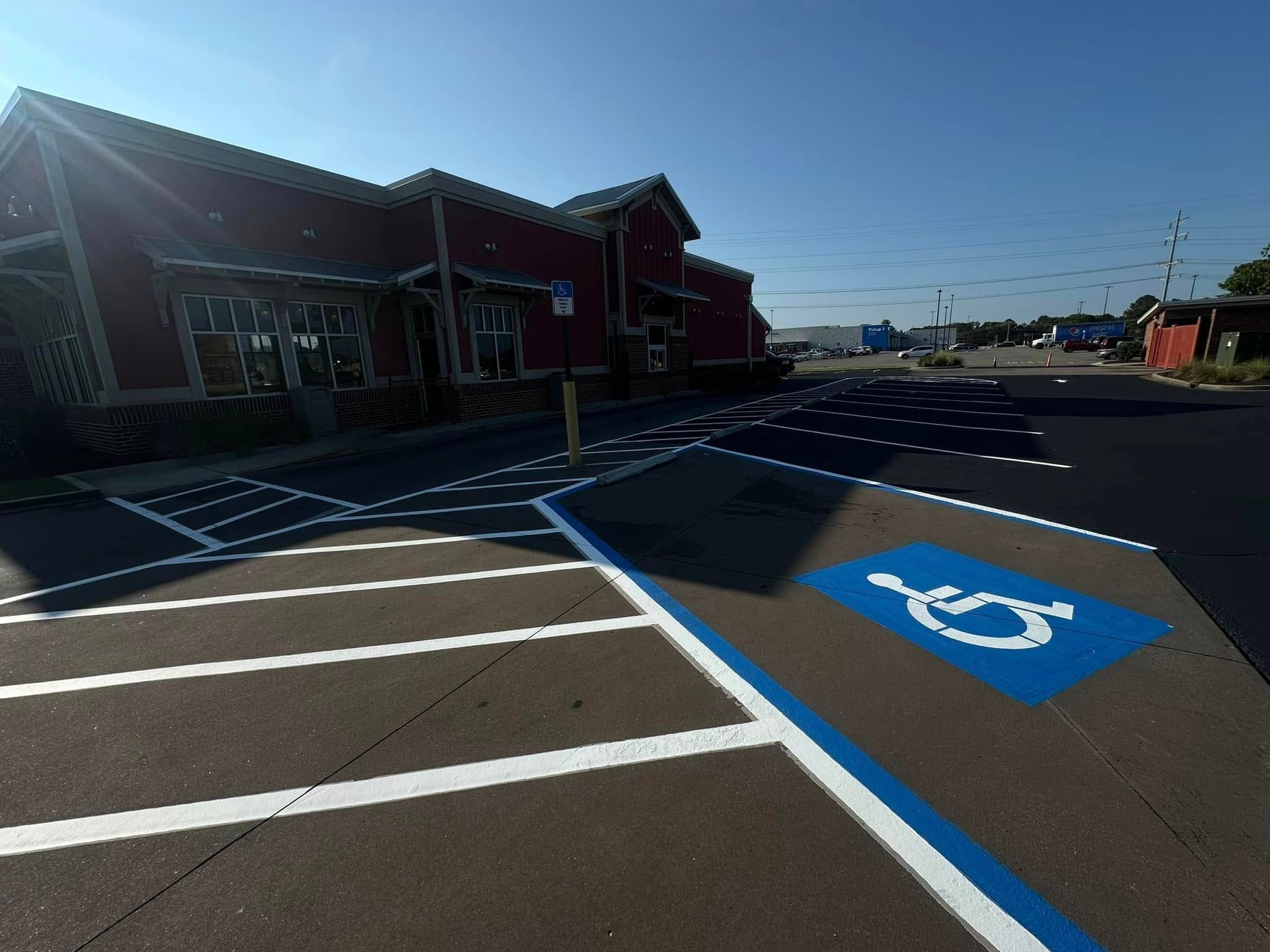 Handicap parking spot painted blue in front of a red building on a sunny day.