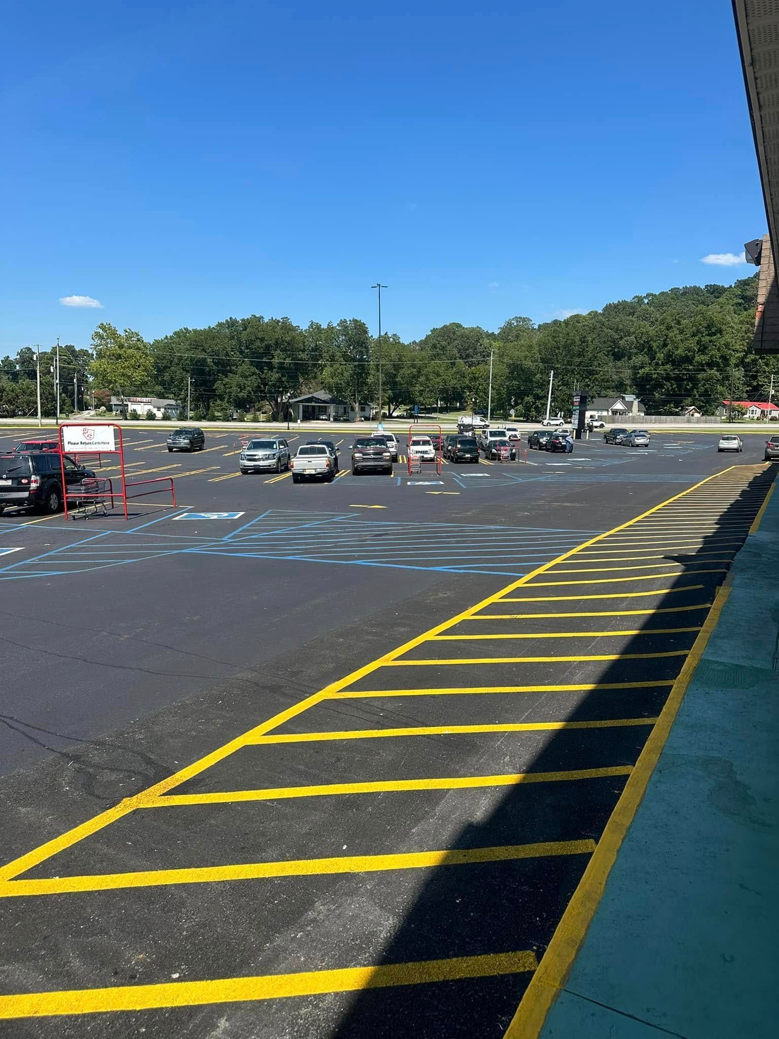 Cars in a parking lot with painted yellow lines. Blue sky, trees in the background.