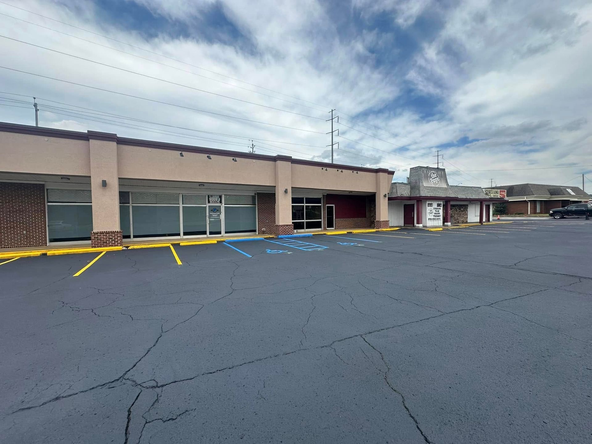 Exterior view of a strip mall with empty storefronts under a cloudy sky.