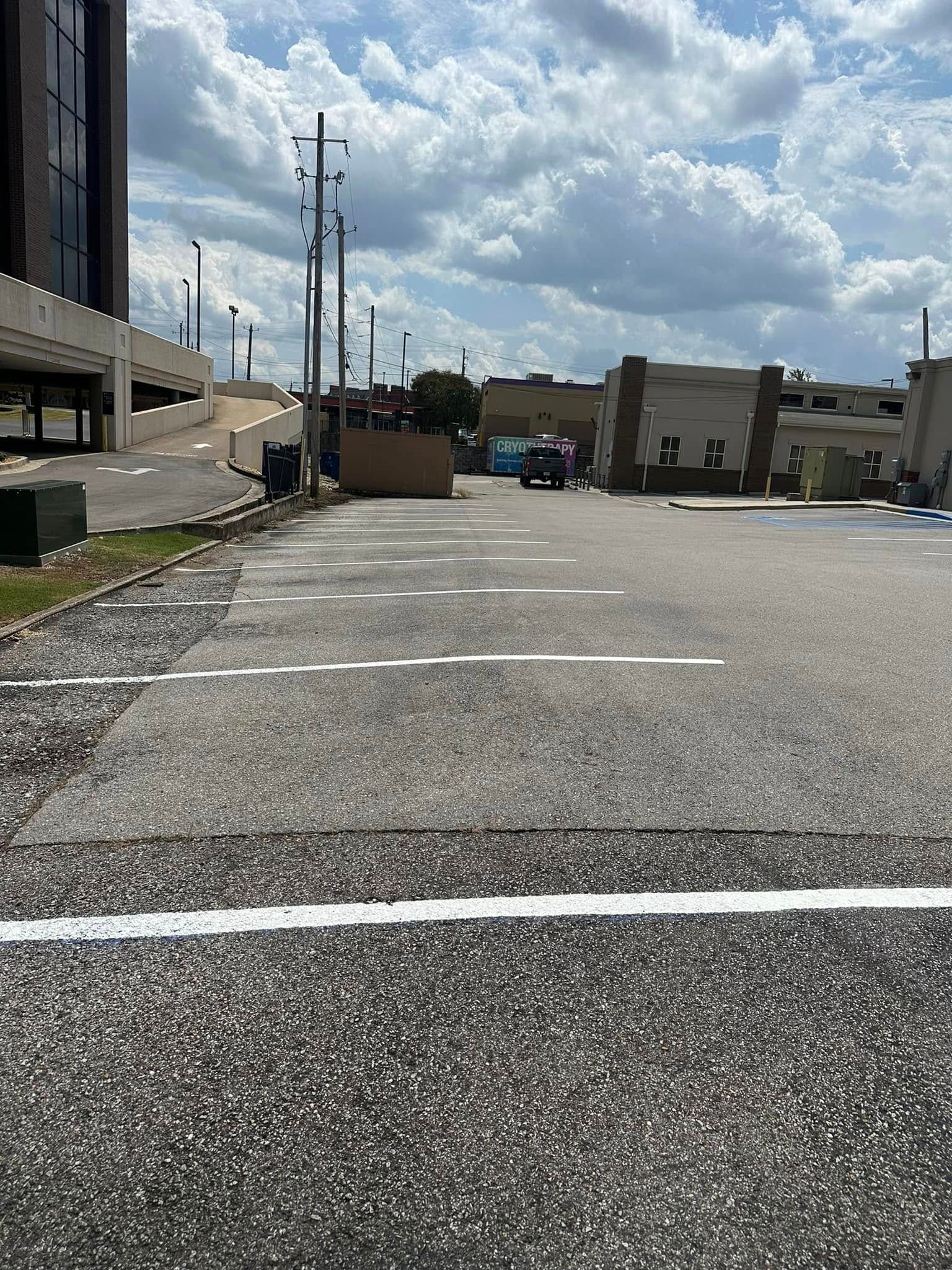 Empty parking lot with white parking space lines under a cloudy sky.