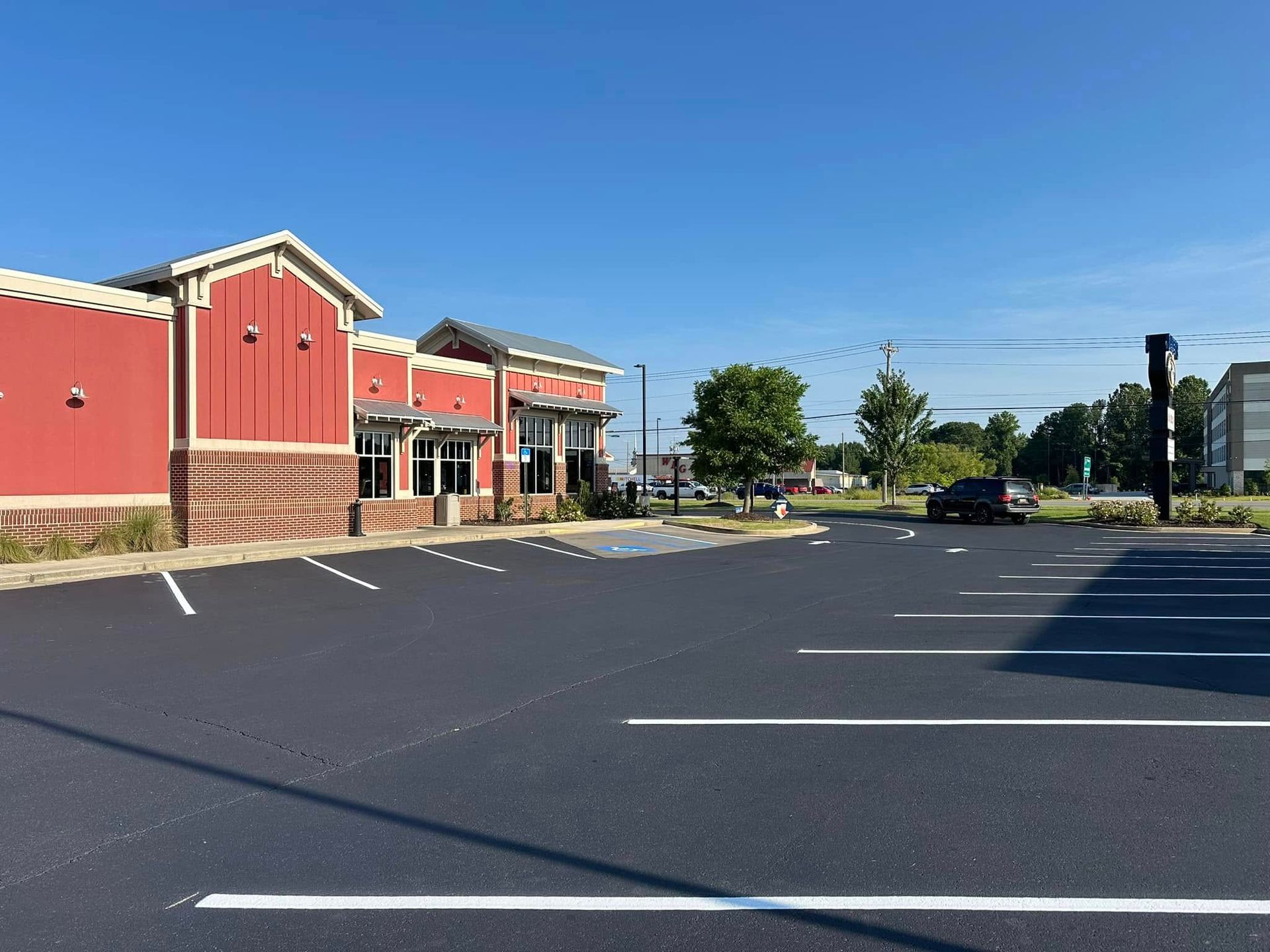Exterior of a restaurant with a red facade and a newly paved parking lot on a sunny day.