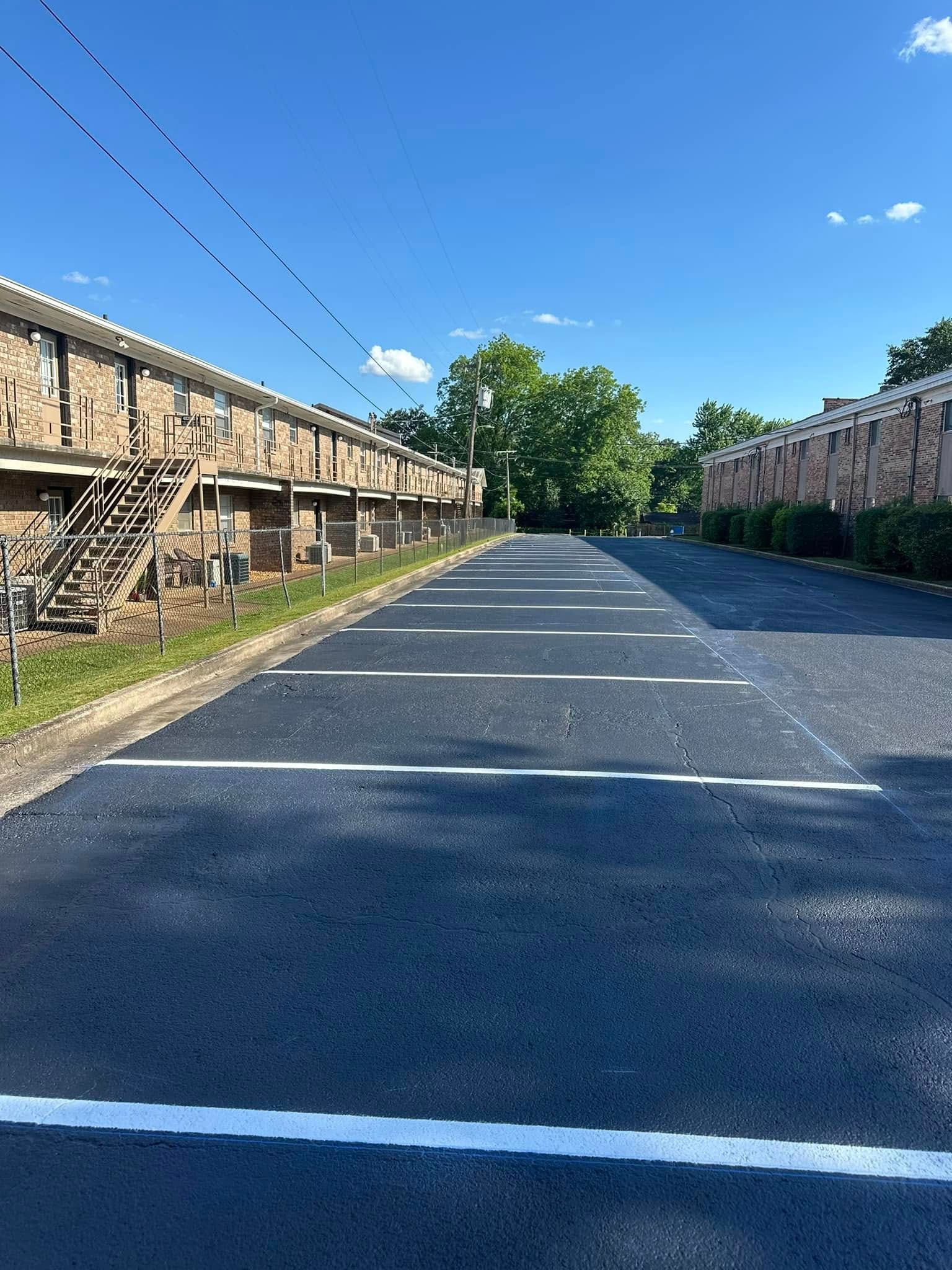 Paved parking area between two brick apartment buildings under a bright blue sky.