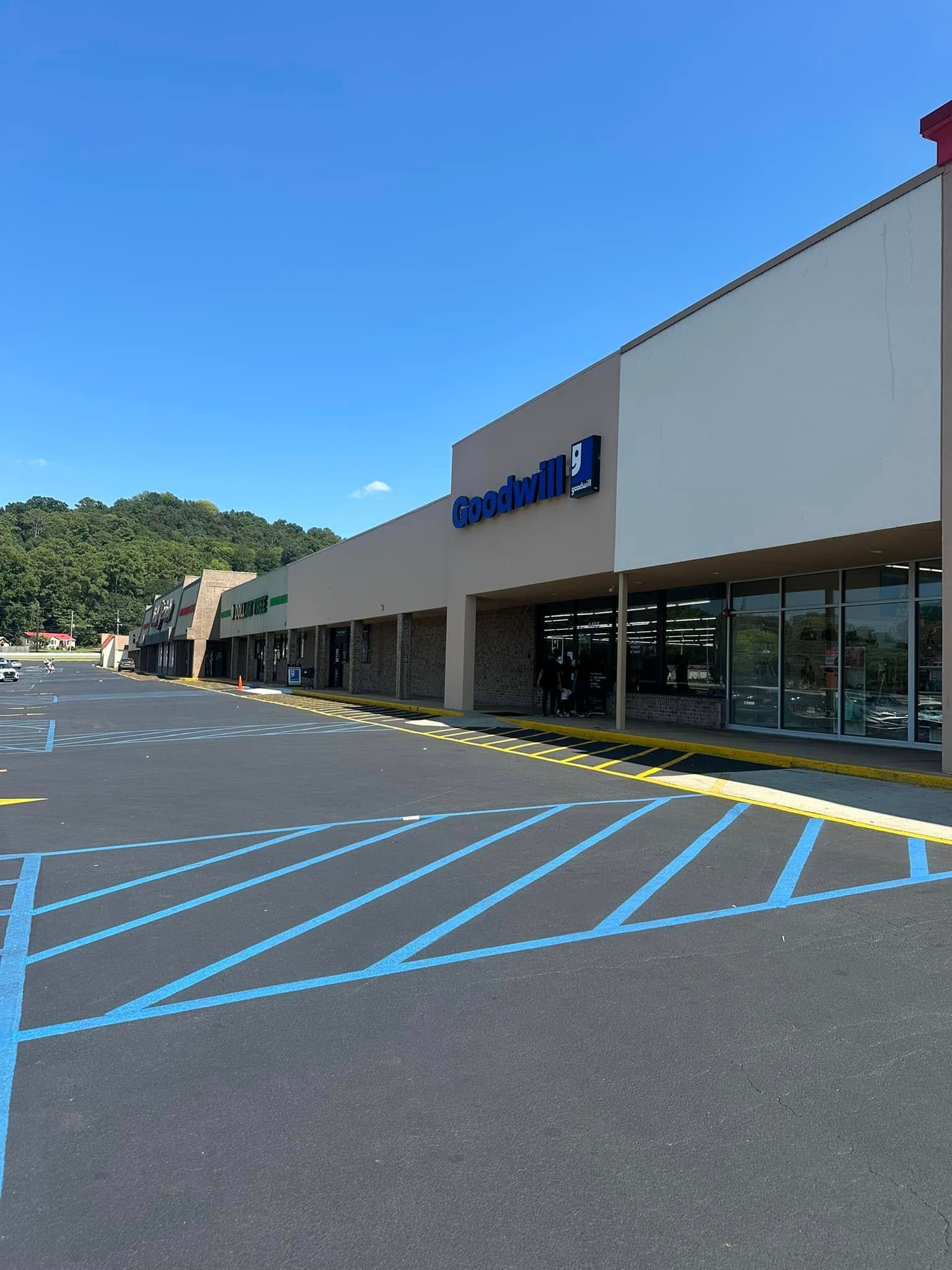Exterior of a Goodwill store in a shopping center on a sunny day with blue parking lines.