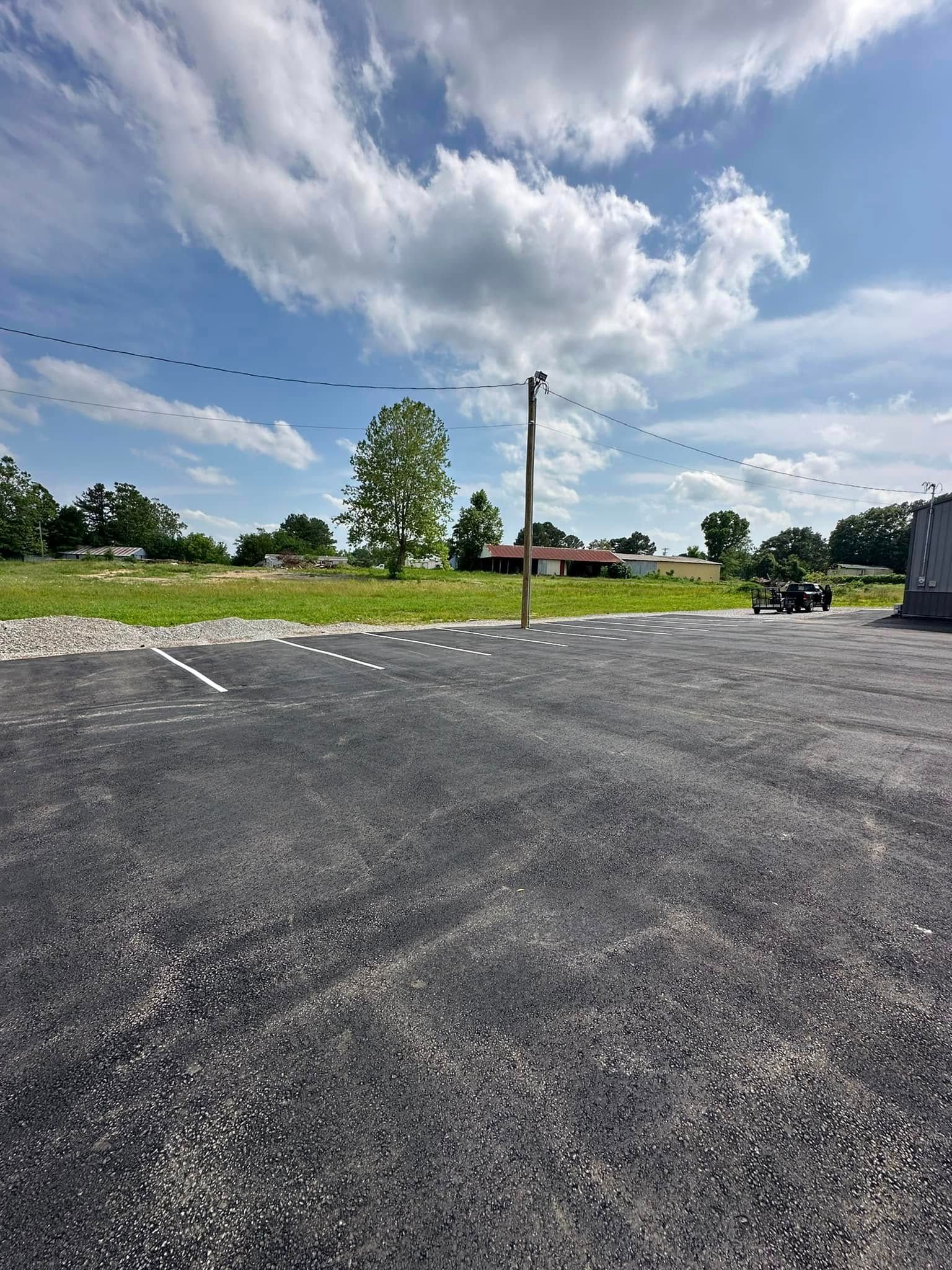 Paved parking lot with a utility pole and a green field under a partly cloudy sky.