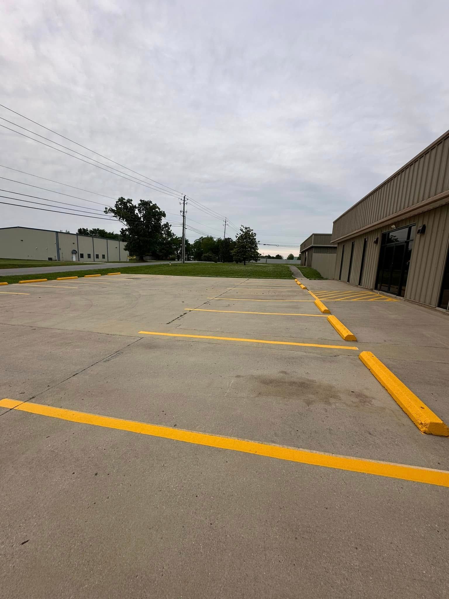 Empty parking lot with yellow painted lines and parking stops beside a building. Overcast sky.