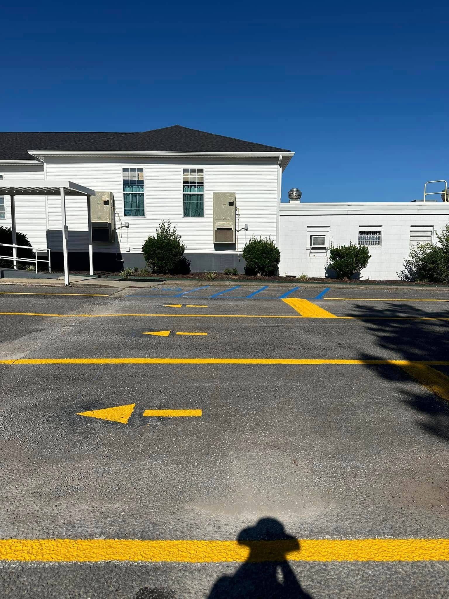 Yellow painted parking arrows and spaces in front of a white building with bushes and blue sky.