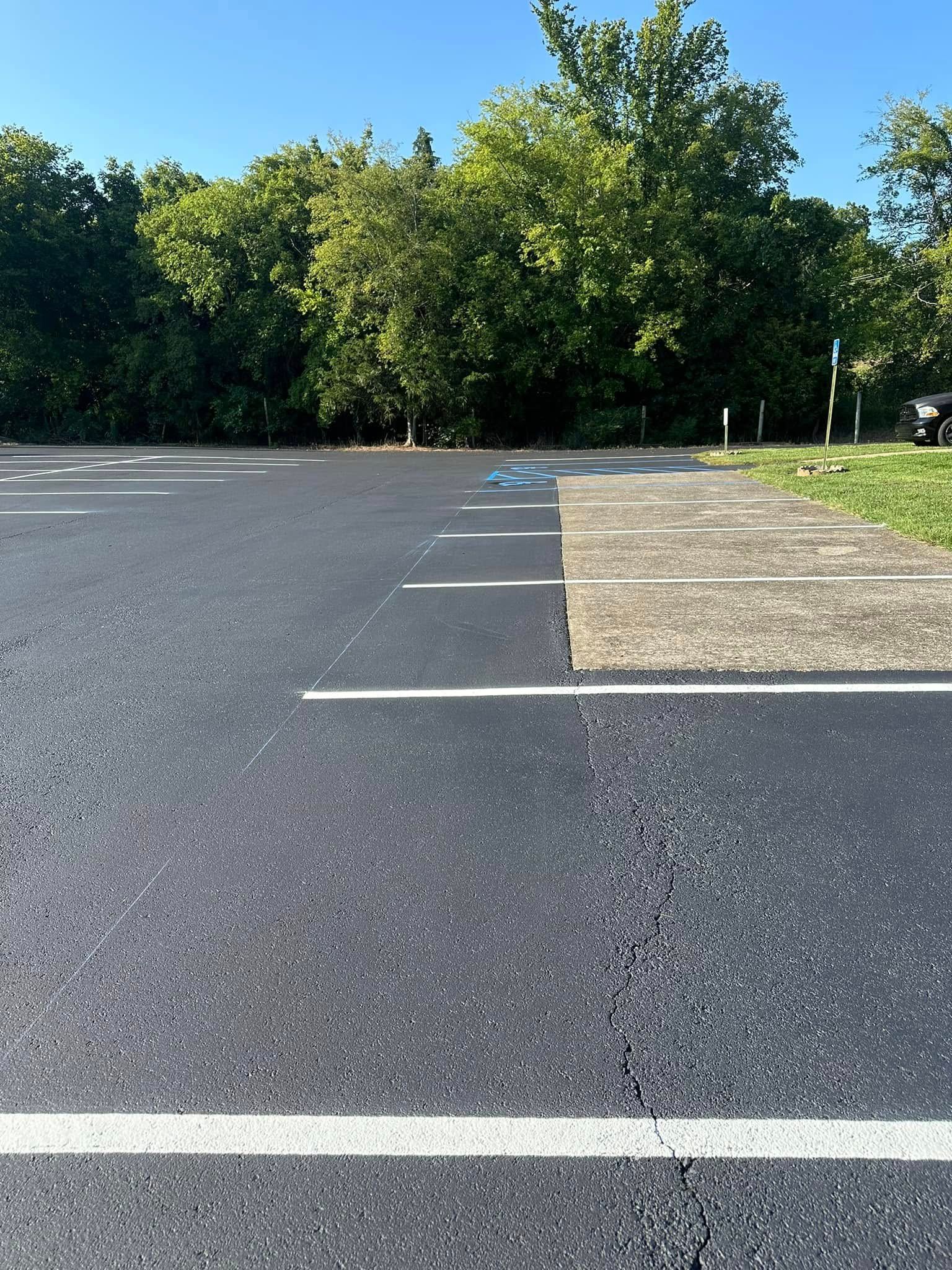 Asphalt parking lot with white lines, concrete sidewalk, trees in background, blue object on pavement.