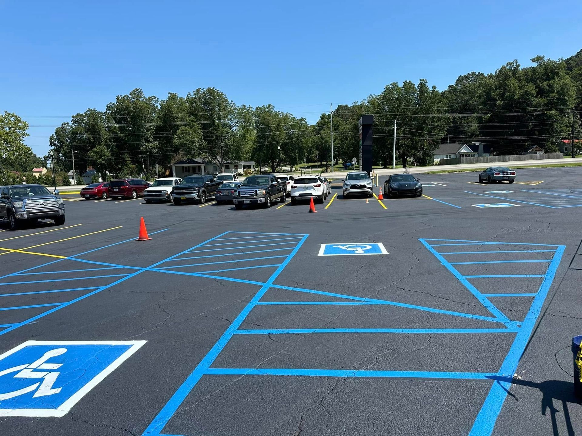 Parking lot with blue and yellow lines. Several cars parked, including accessible parking spaces. Sunny day.