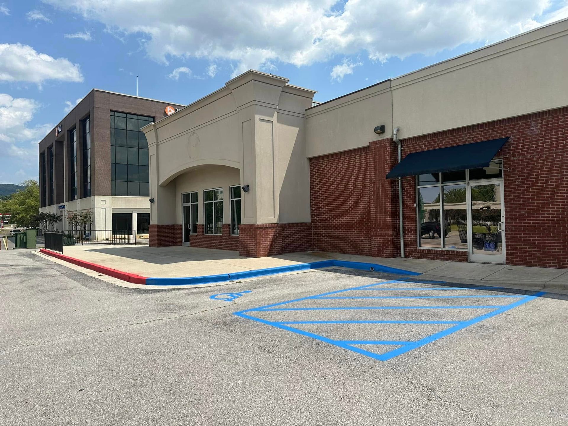 Exterior of a commercial building with brick and beige facades, handicap parking, and a blue awning.