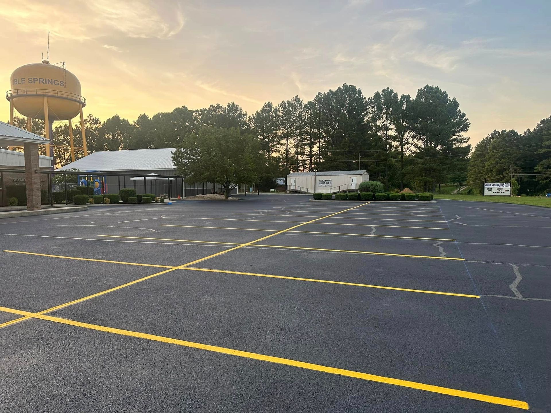 Empty parking lot with yellow lines, a water tower, and a building under a sunset sky.