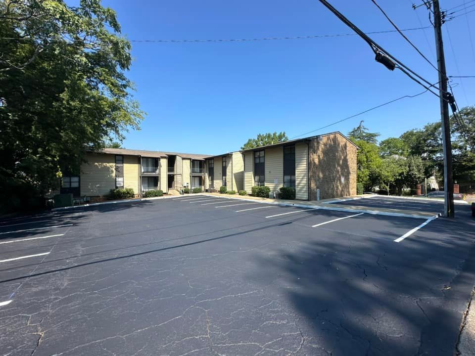 Apartment building with asphalt parking lot, blue sky, and trees.