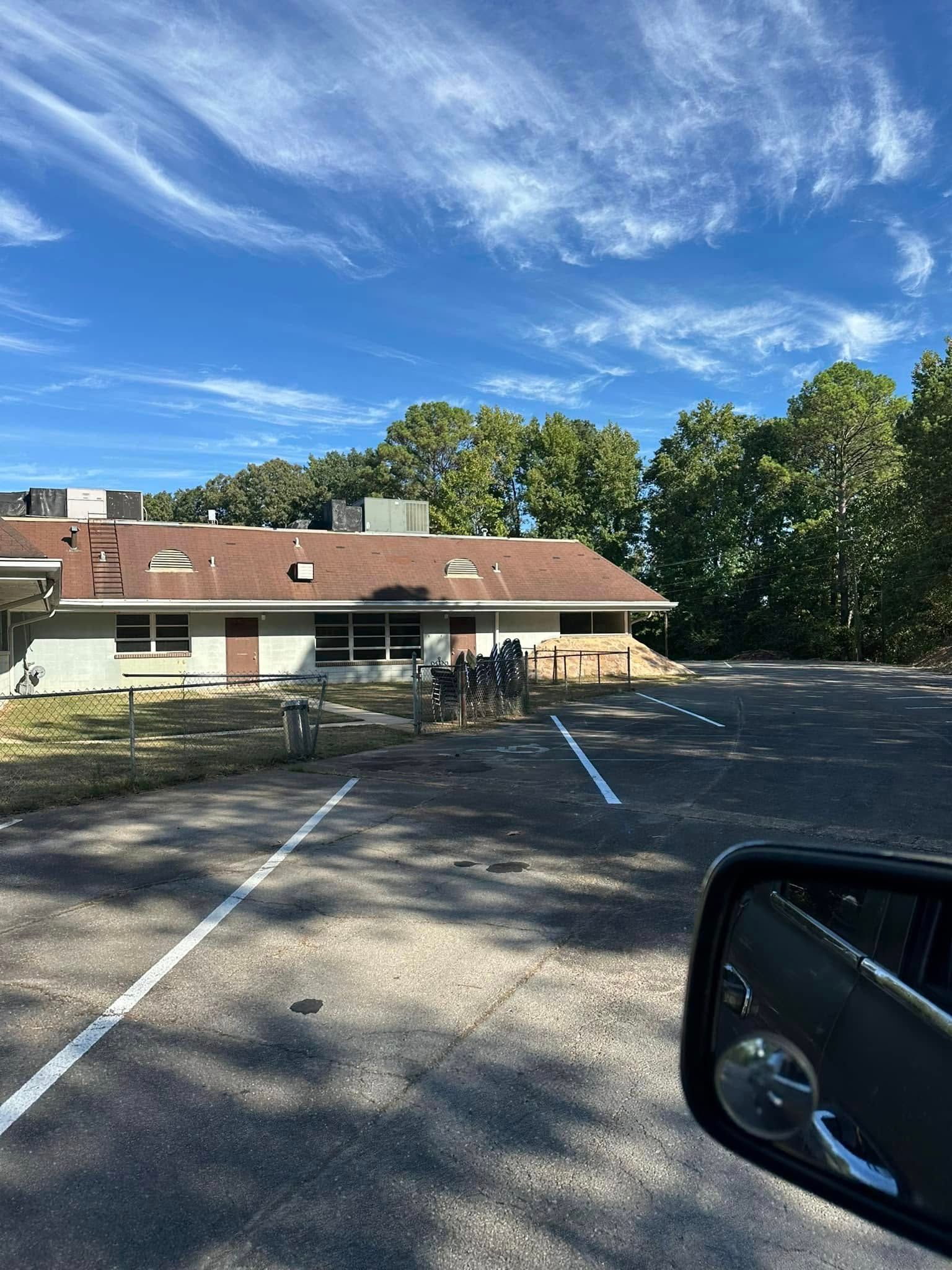 Building with brown roof, parking lot, trees, and blue sky.
