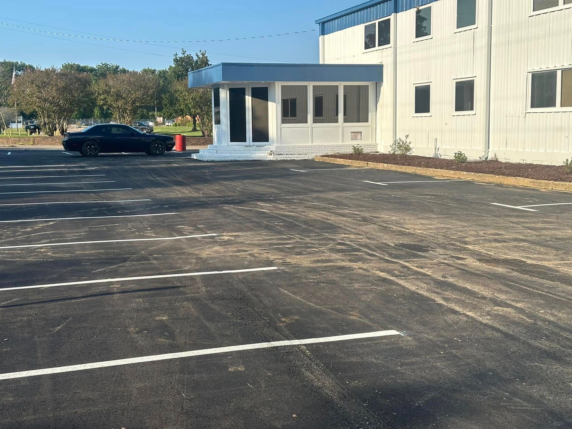 A black car parked near a blue-trimmed building with a covered entrance. Asphalt parking lot.