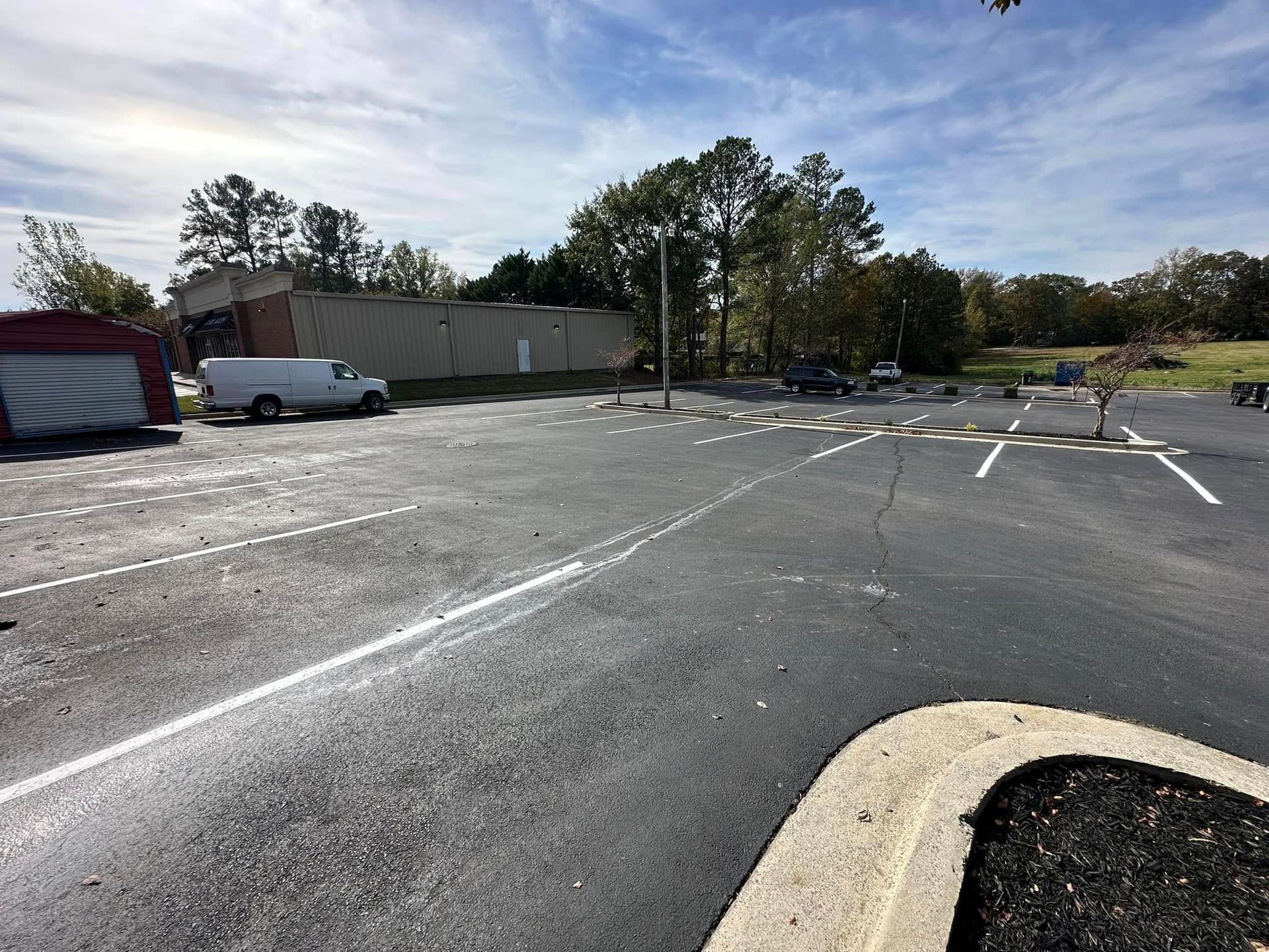 Asphalt parking lot with white lines; van, cars, and building in background; sunny day.