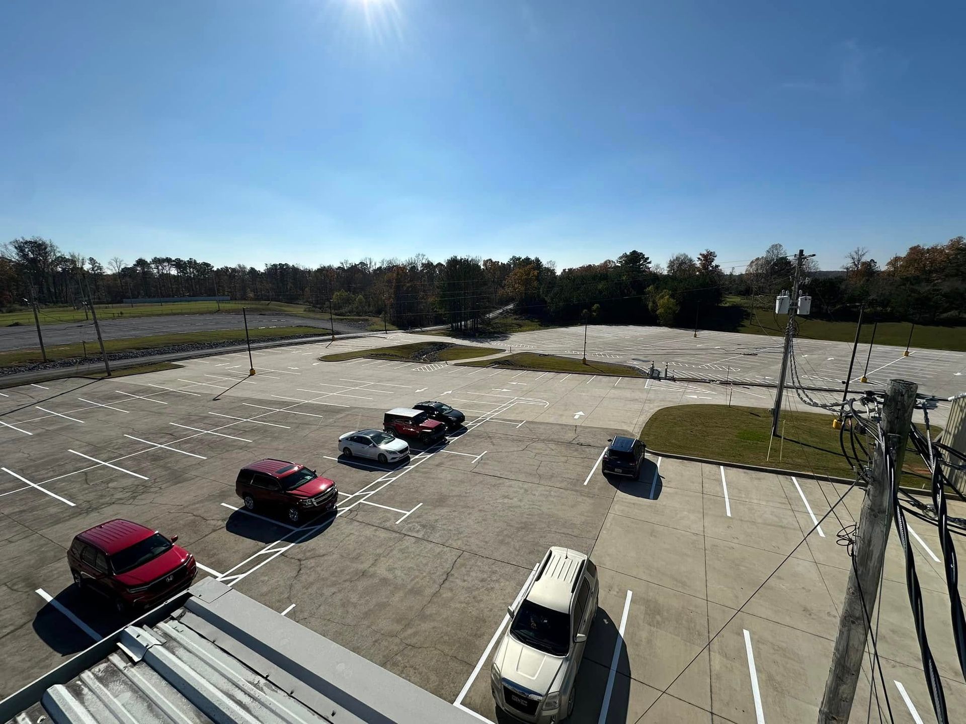 A mostly empty parking lot with several parked cars under a bright, sunny sky.