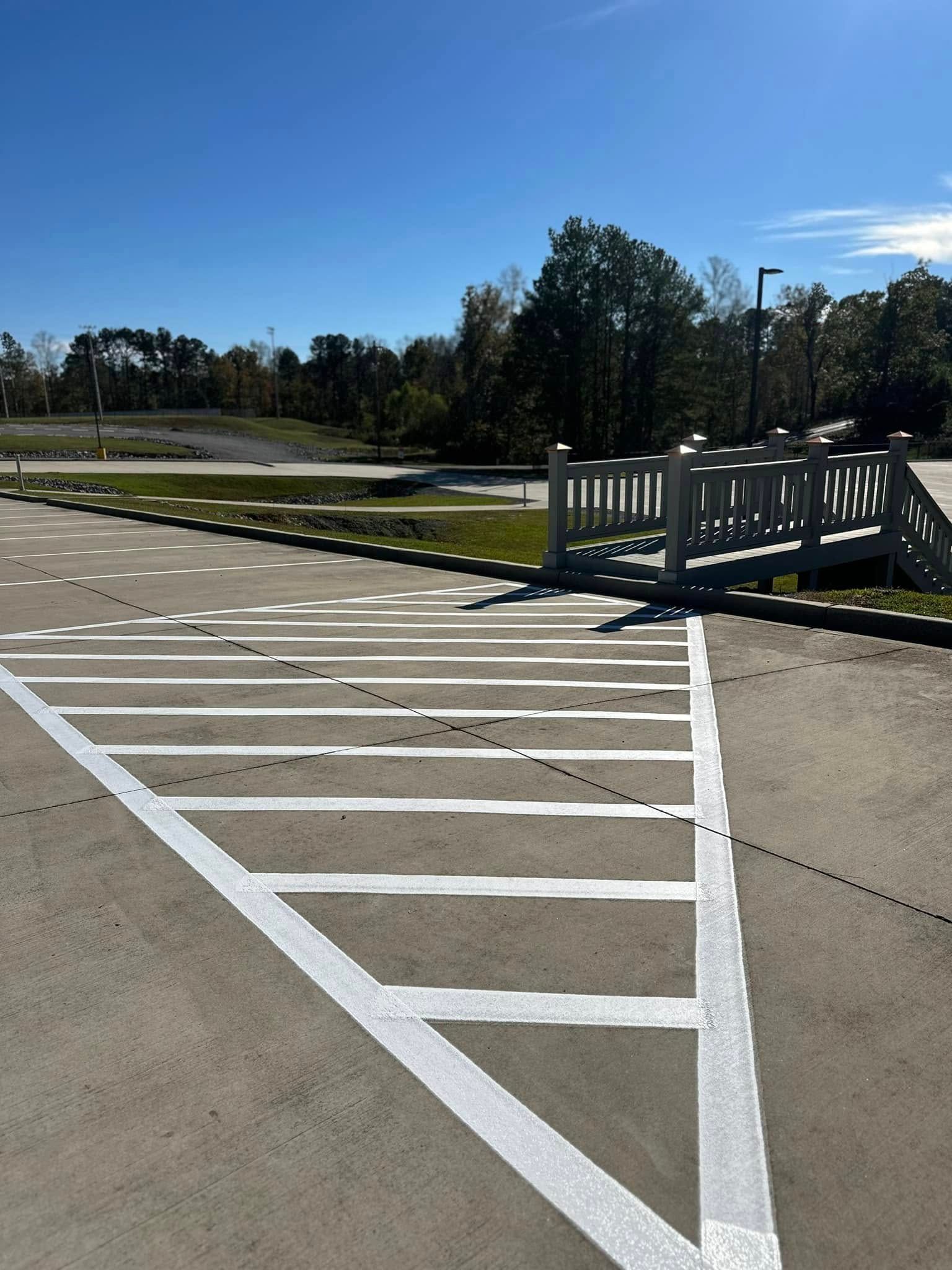 White painted lines on asphalt leading to a bridge with a green space and blue sky in the background.