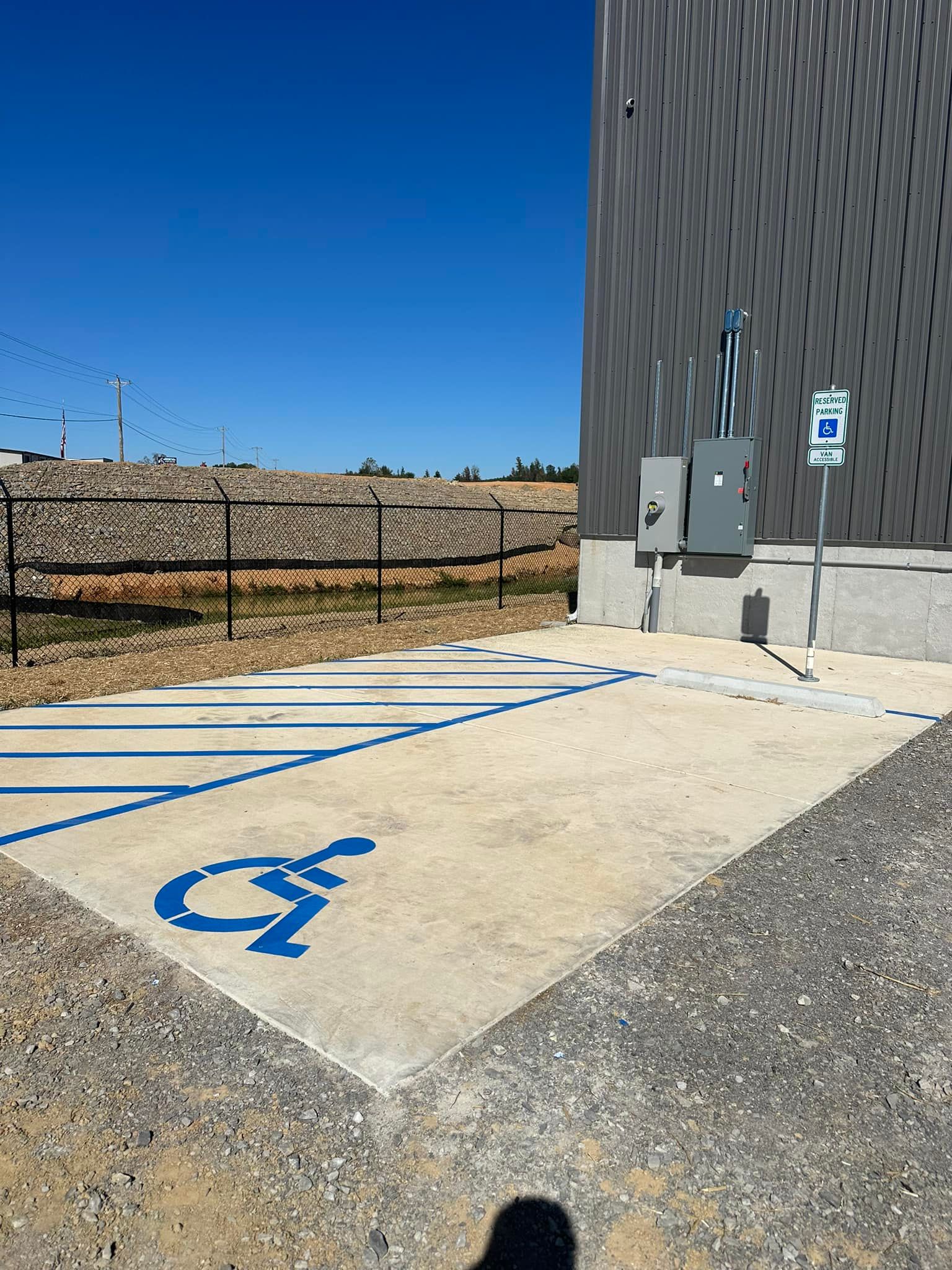 Accessible parking space with blue wheelchair symbol, next to building with power supply and sign, on a sunny day.
