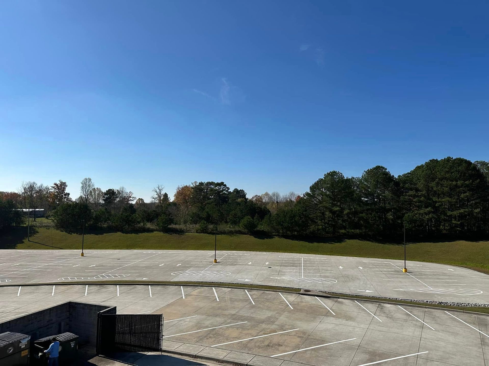 Empty parking lot, green grass, and trees under a clear blue sky.