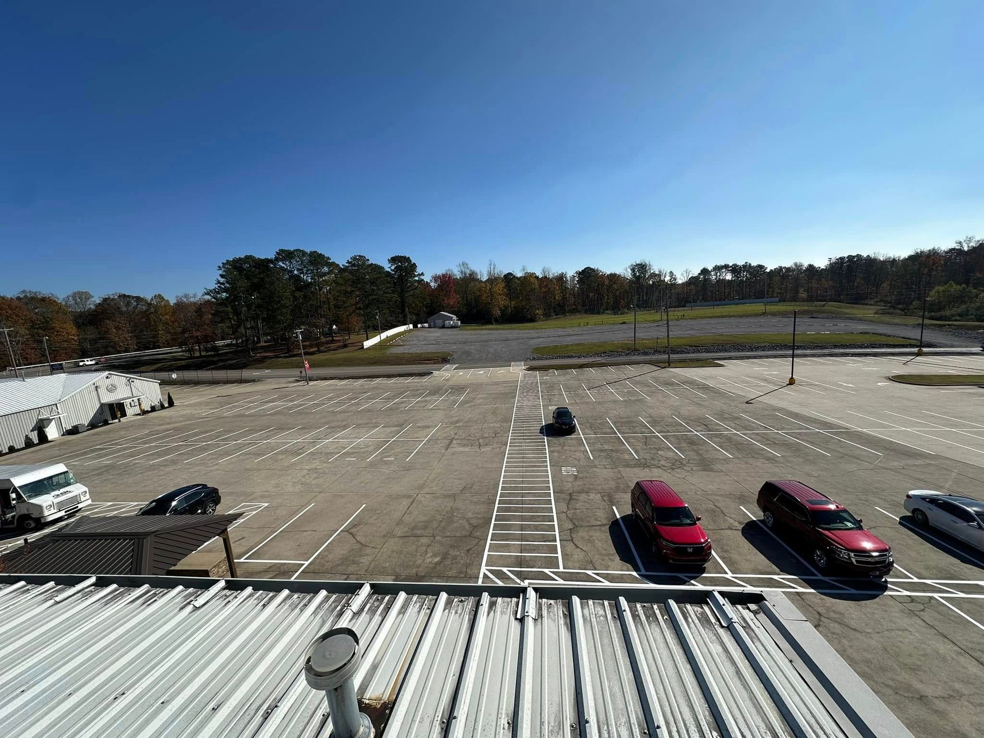 Cars parked in a mostly empty parking lot under a clear, blue sky. Trees in the background.