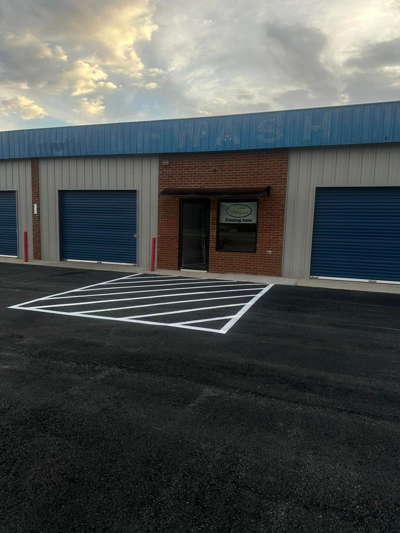 Storage units with blue doors, asphalt, and a patterned walkway.
