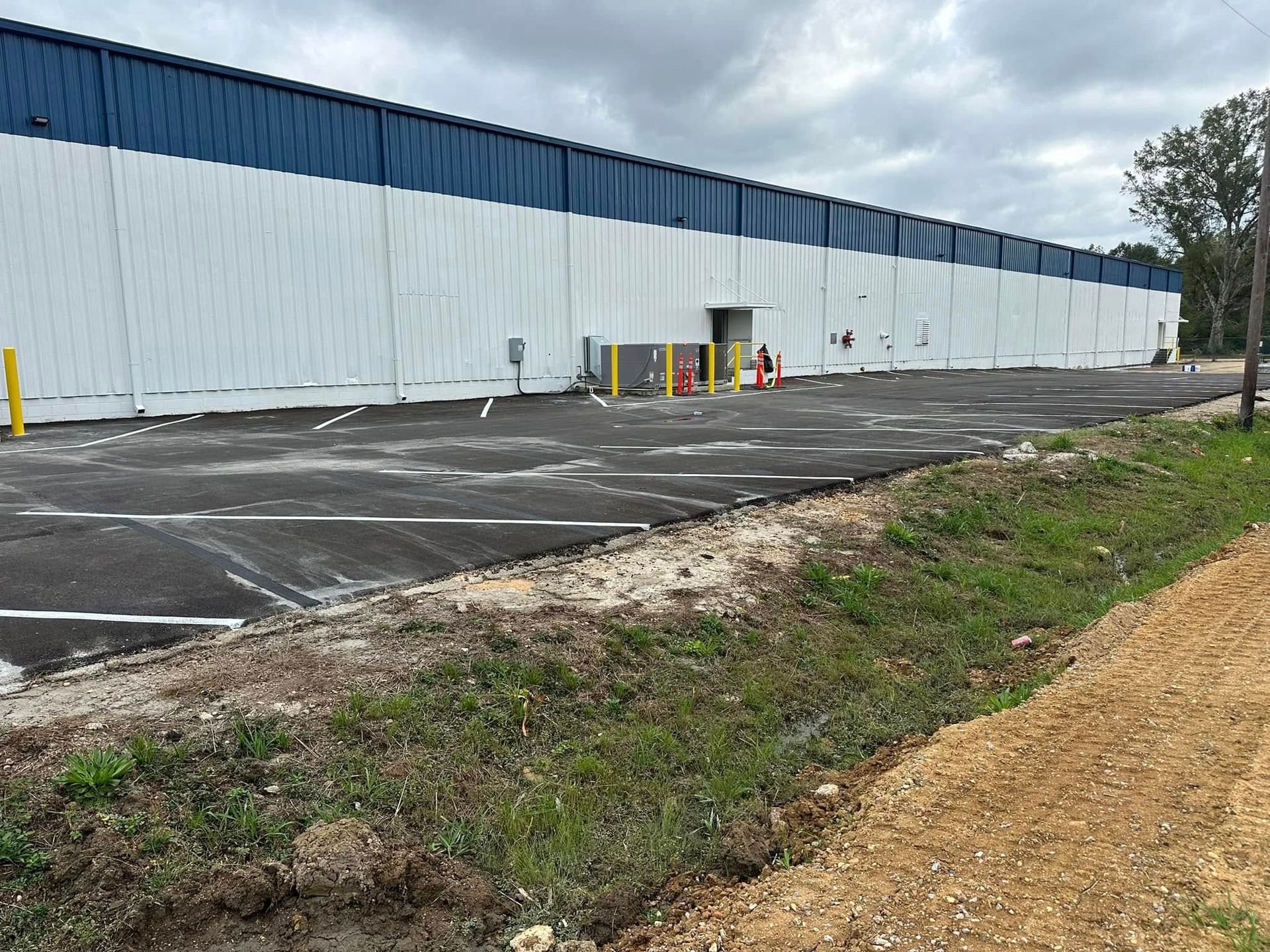 Exterior view of a commercial building with a blue and white facade. Asphalt parking lot in front with grassy edge.