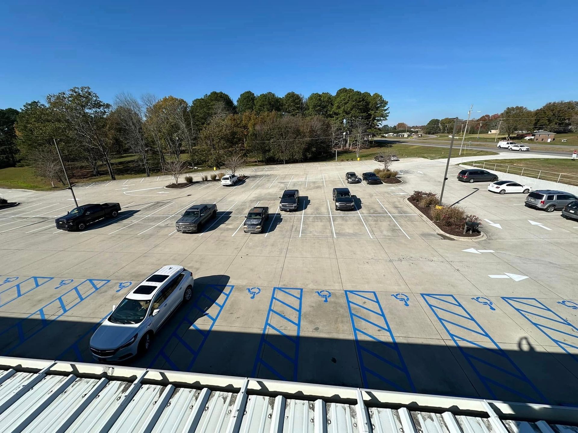 Cars parked in a mostly empty parking lot on a sunny day with trees in the background.