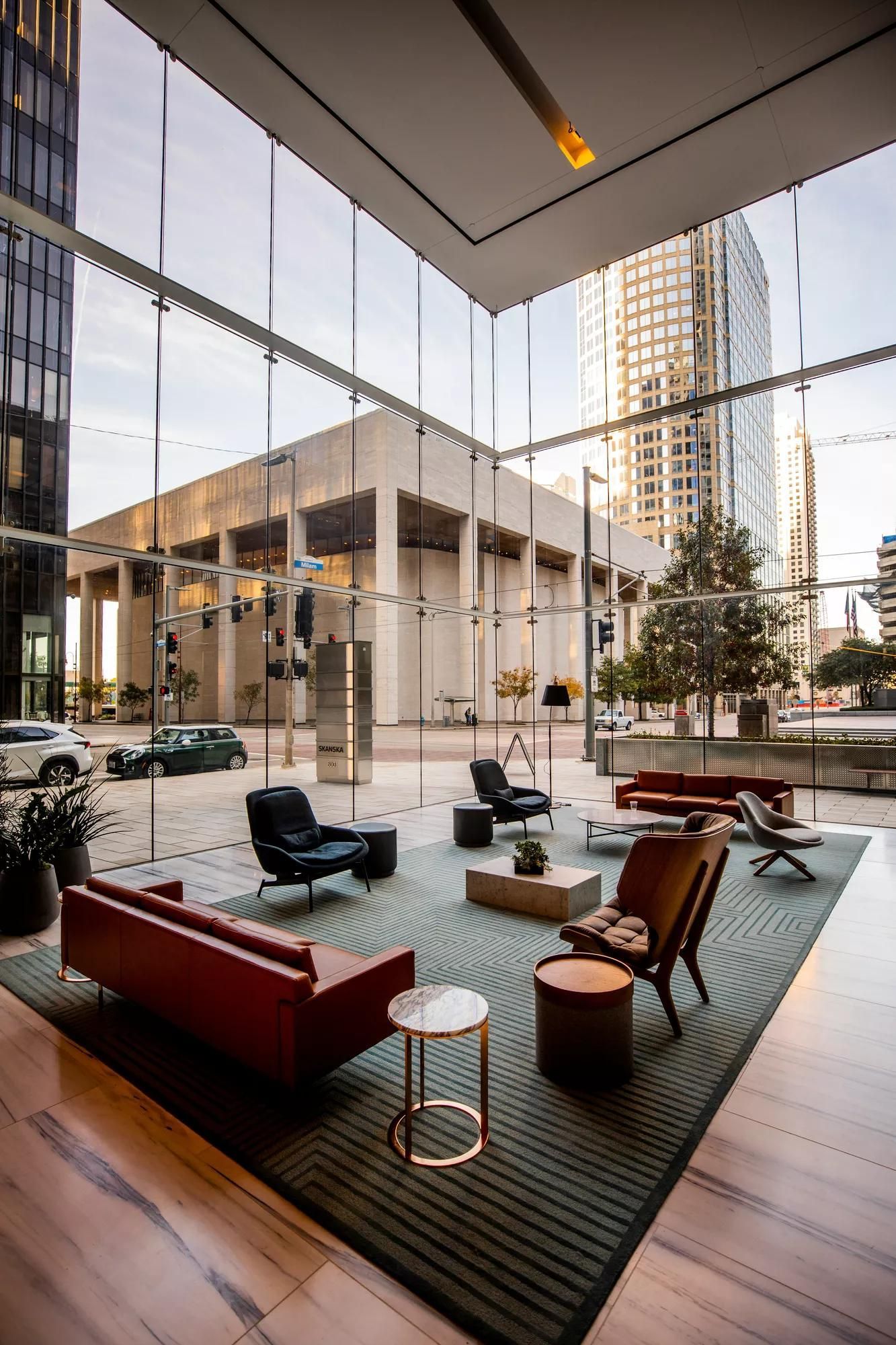 Modern hotel lobby with glass walls, lounge seating, and city view