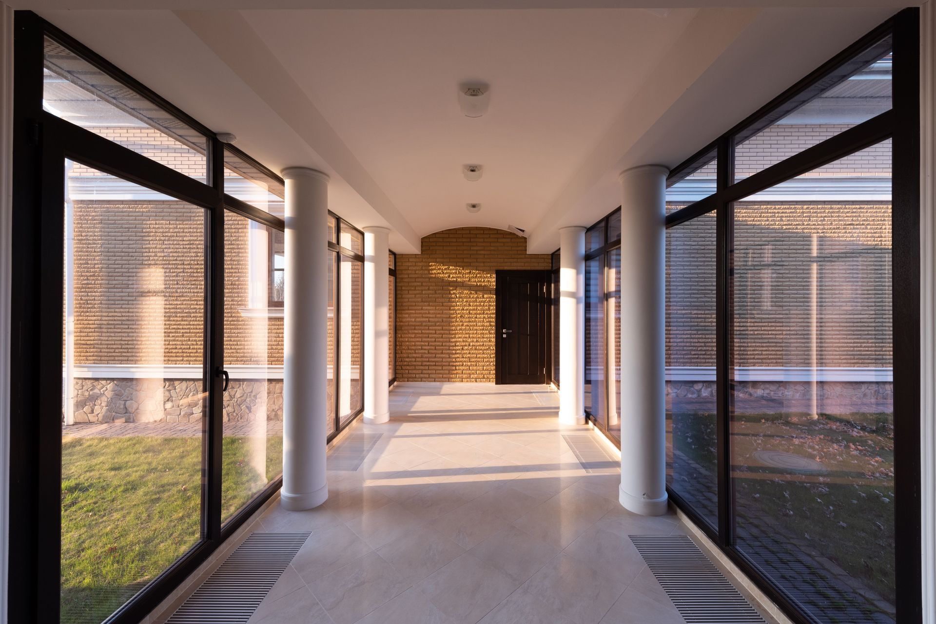 Modern indoor corridor with large glass windows and a sunlit brick wall at the end