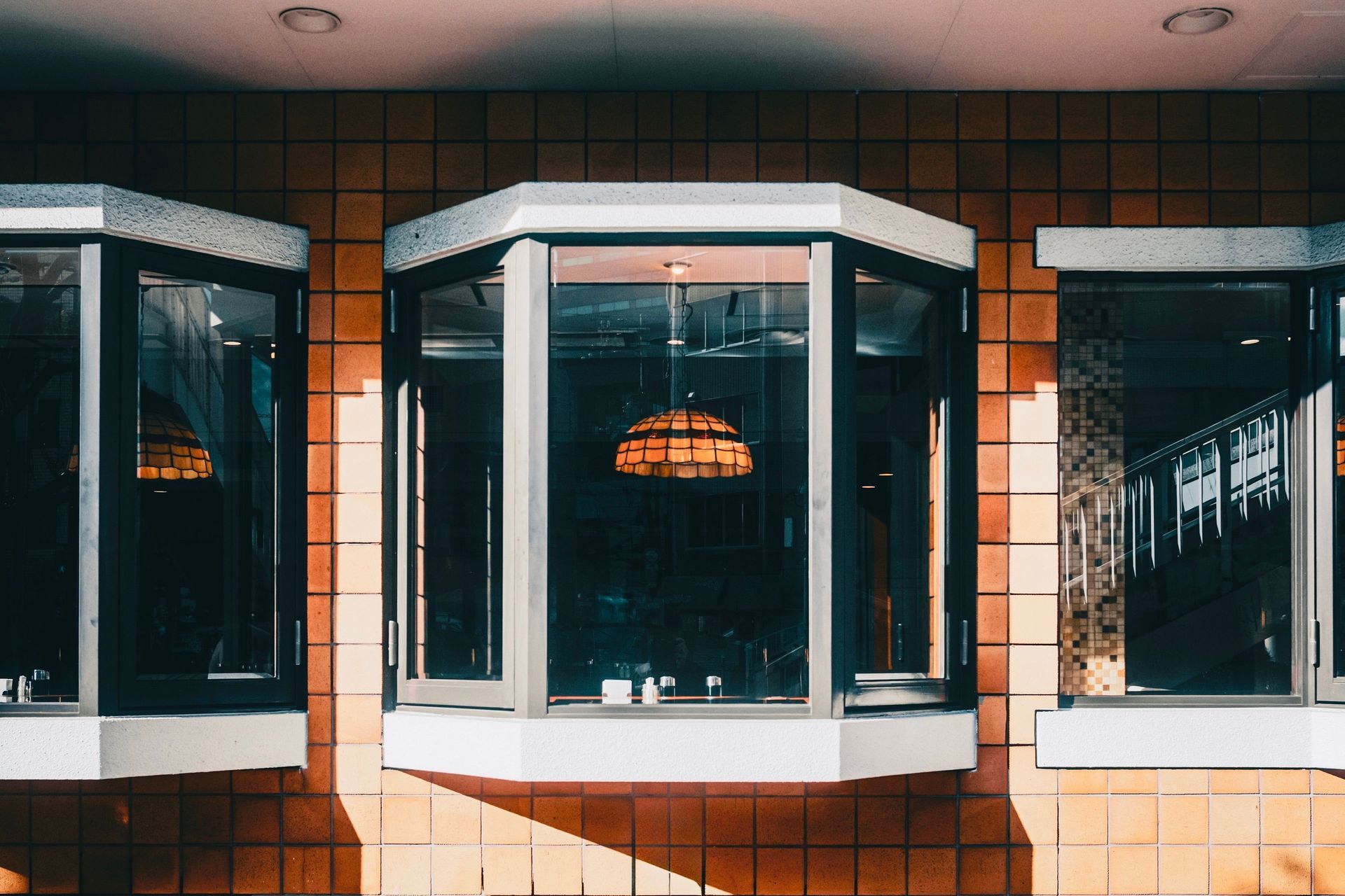 Storefront windows with white trim and warm reflections on a tiled exterior wall