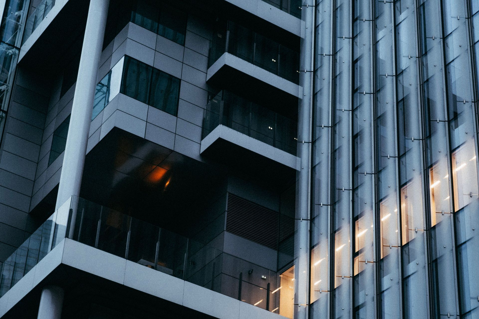 Modern building facade with geometric balconies and reflective glass windows in cool blue-gray tones