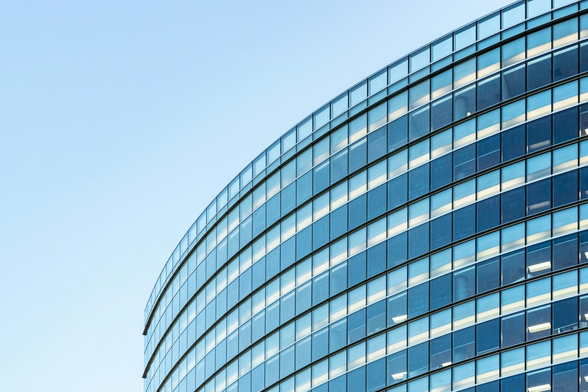 Curved glass office building facade against a clear blue sky