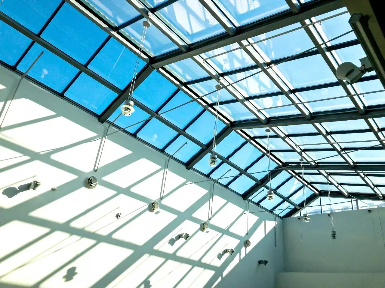 Glass ceiling with blue skylights and hanging lights casting shadows on white walls